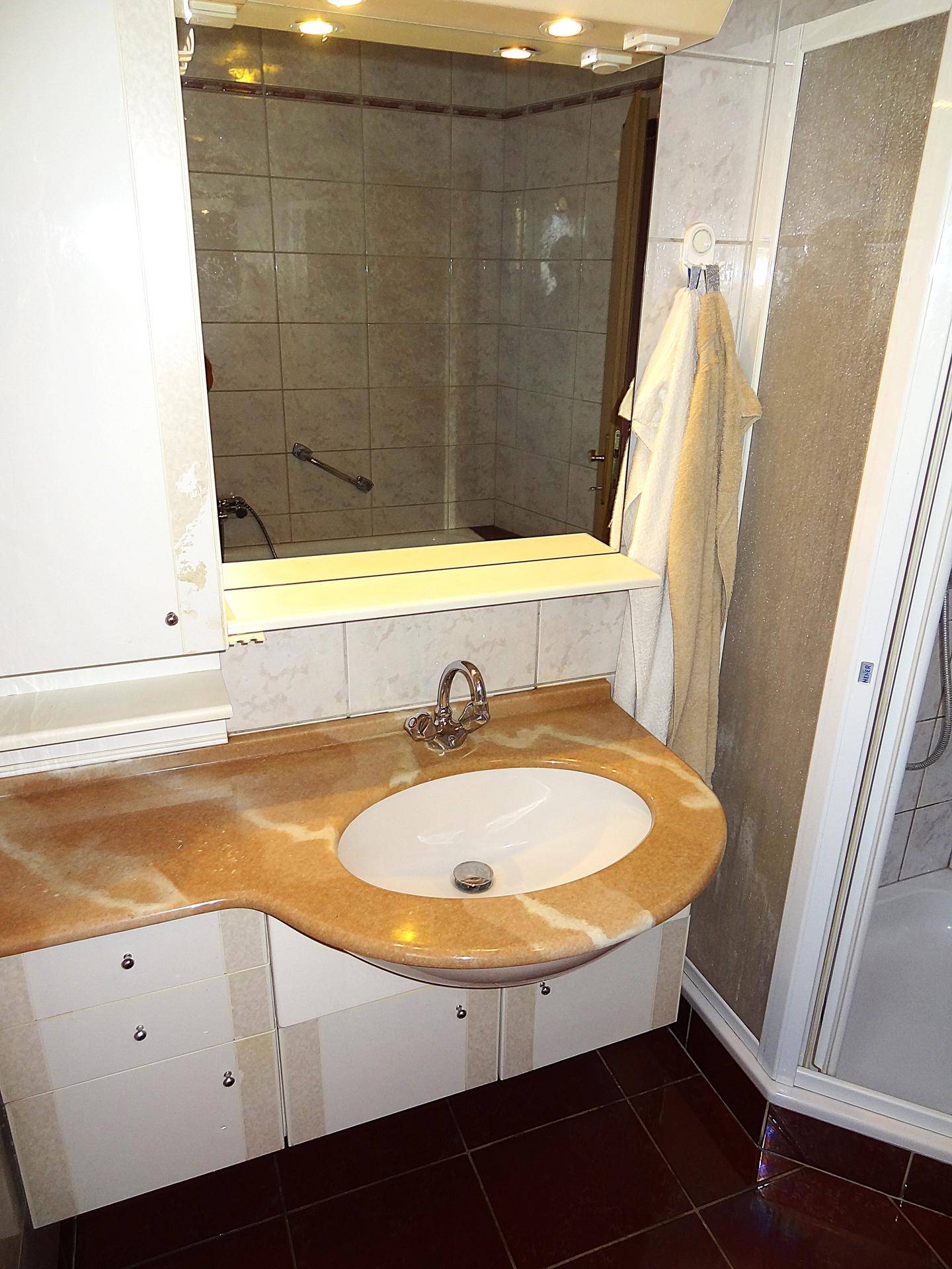 Badezimmer mit Waschbecken, Spiegelschrank und Duschkabine, in hellem Design.