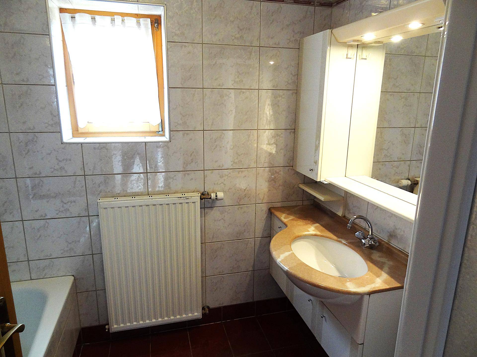 Badezimmer mit Waschbecken, Spiegelschrank, Badewanne und Fenster.