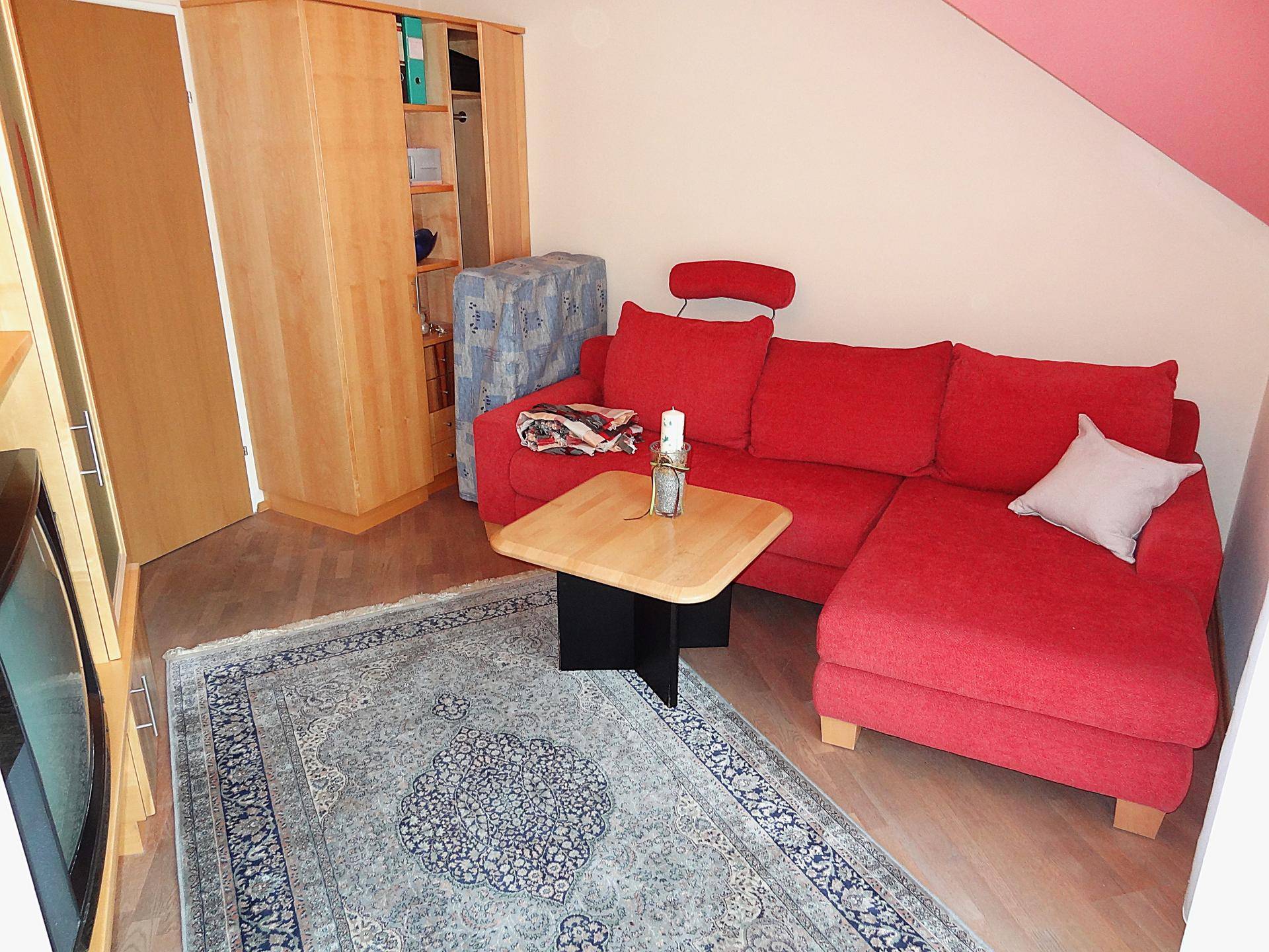 Gemütliches Wohnzimmer mit rotem Sofa, Teppich und Holzschrank.