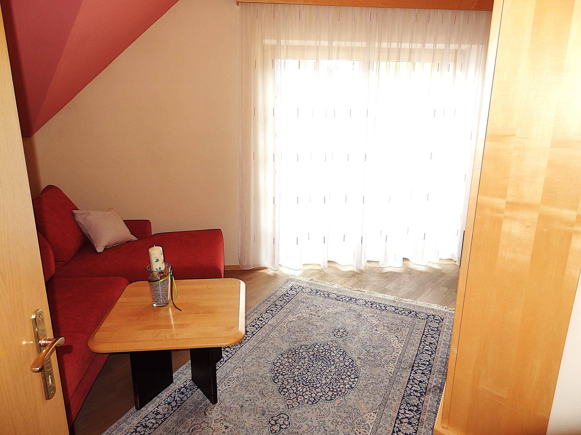 Helles Wohnzimmer mit rotem Sofa, Teppich und großem Fenster.