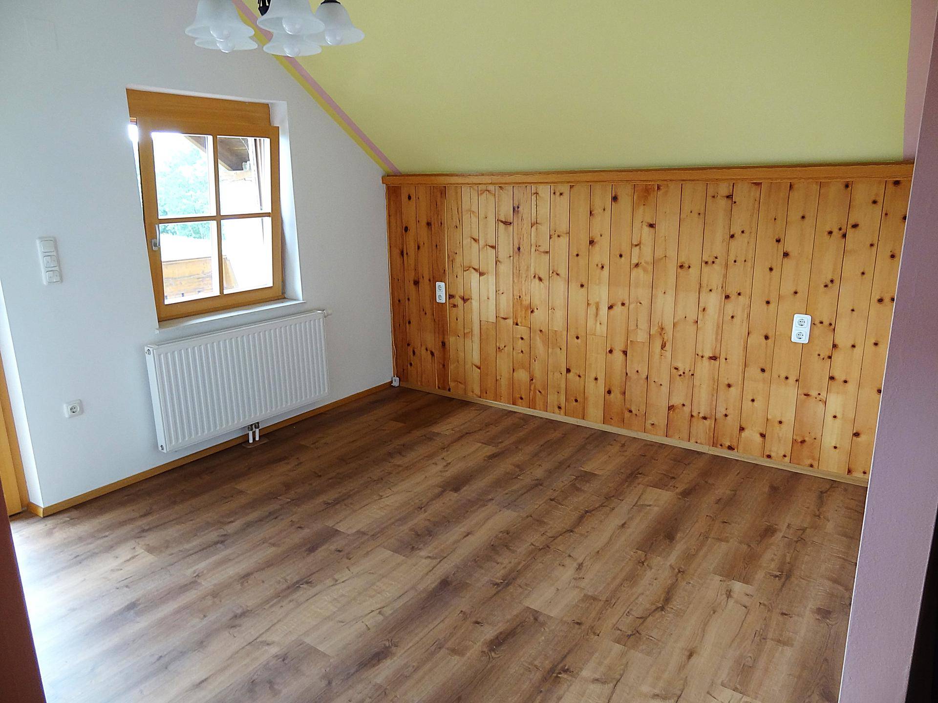 Geräumiges Schlafzimmer mit Holzwandverkleidung und Laminatboden.