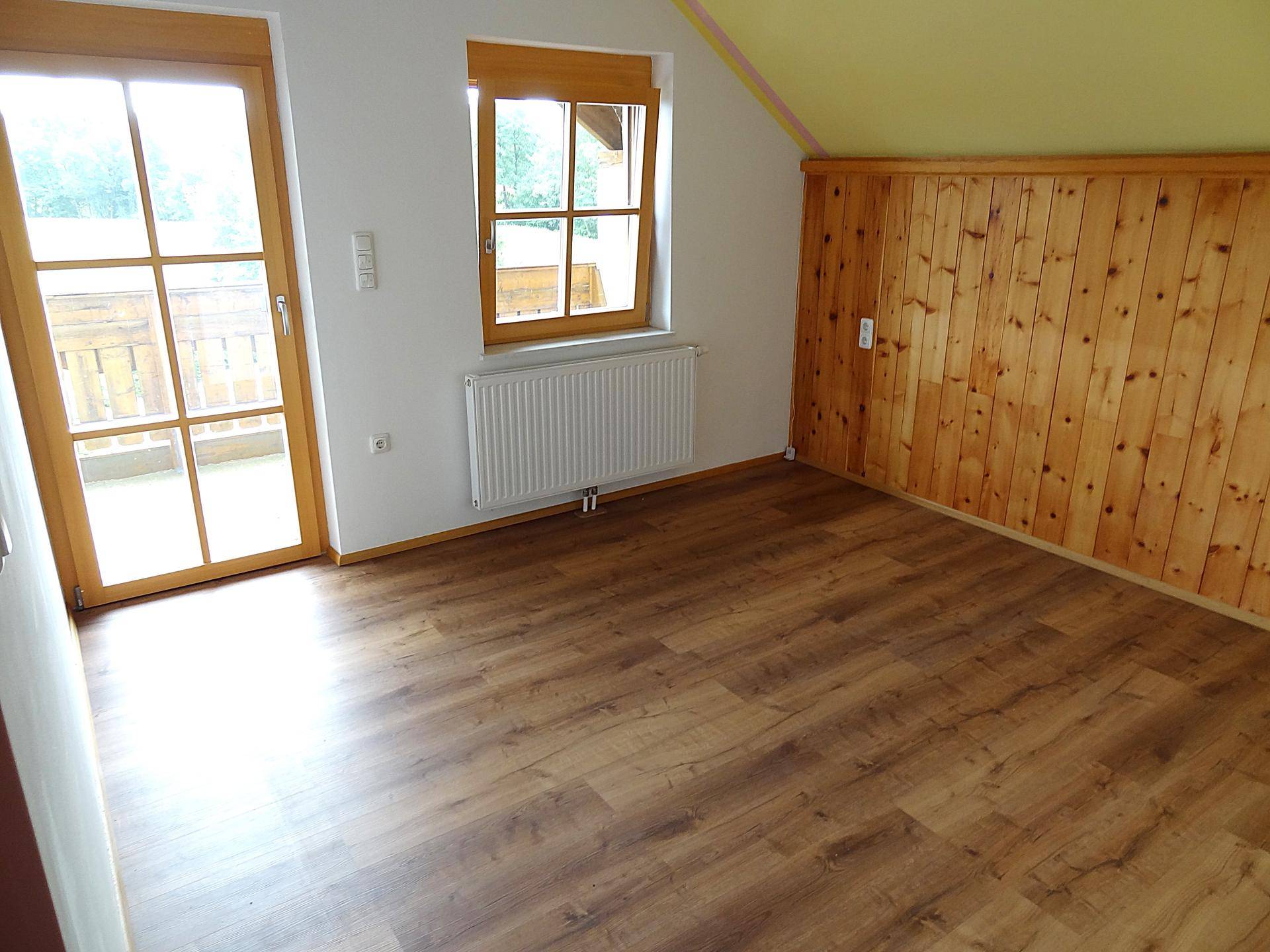 Helles Schlafzimmer mit Holzwand, Laminatboden und Zugang zum Balkon.