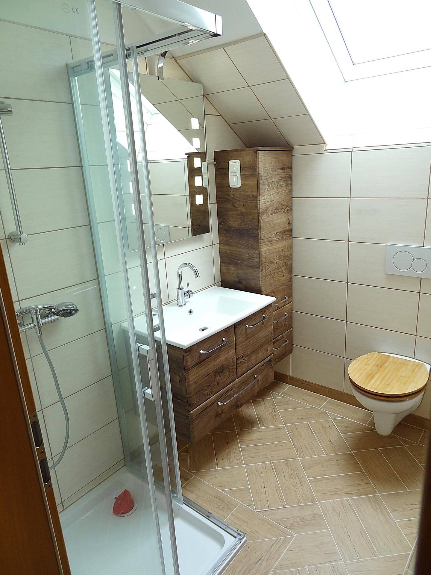 Helles Badezimmer mit Duschkabine, Waschtisch und WC unter Dachschräge.