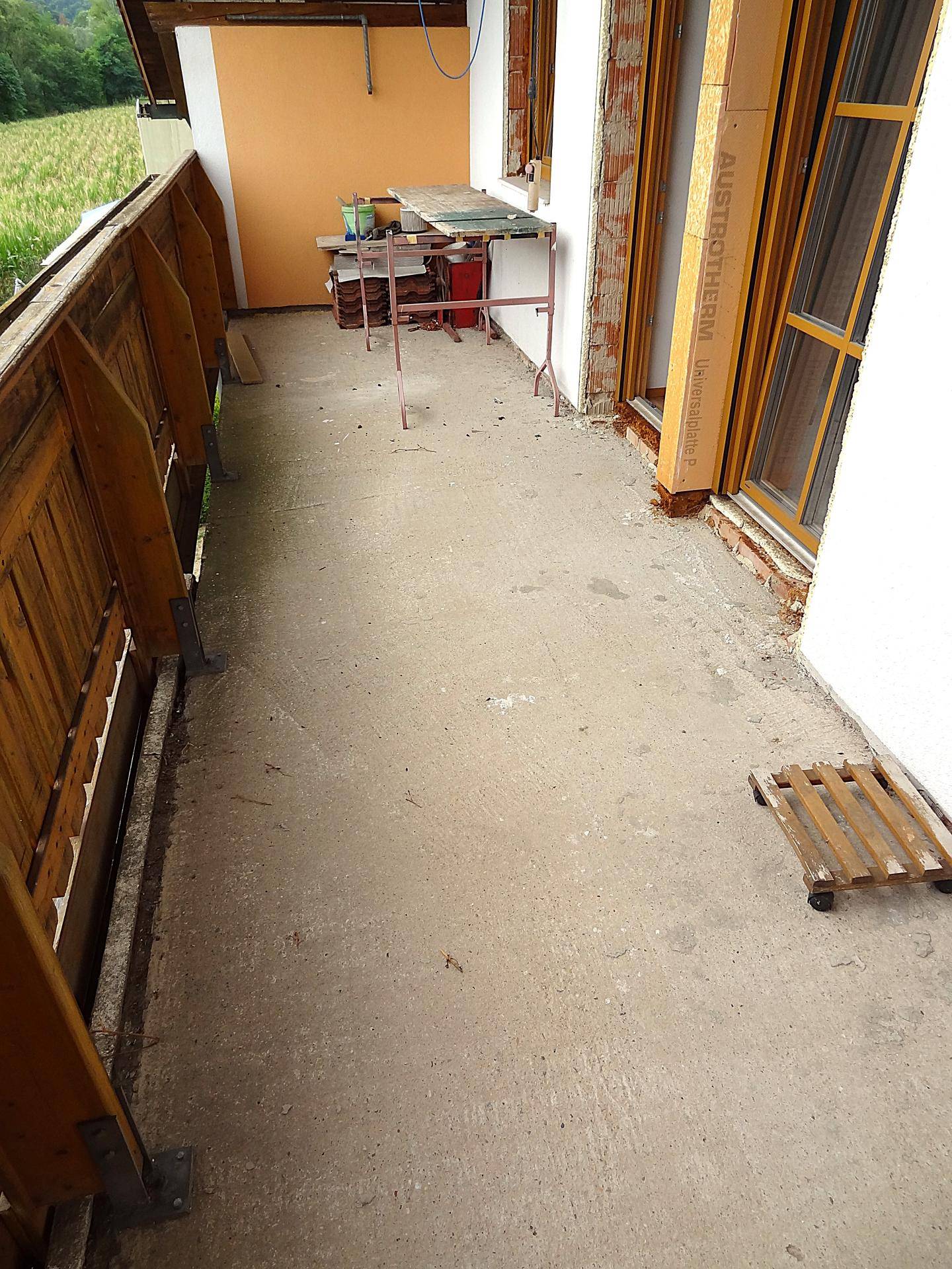 Geräumige Terrasse mit Betonboden und Holzgeländer, bietet viel Platz im Freien.