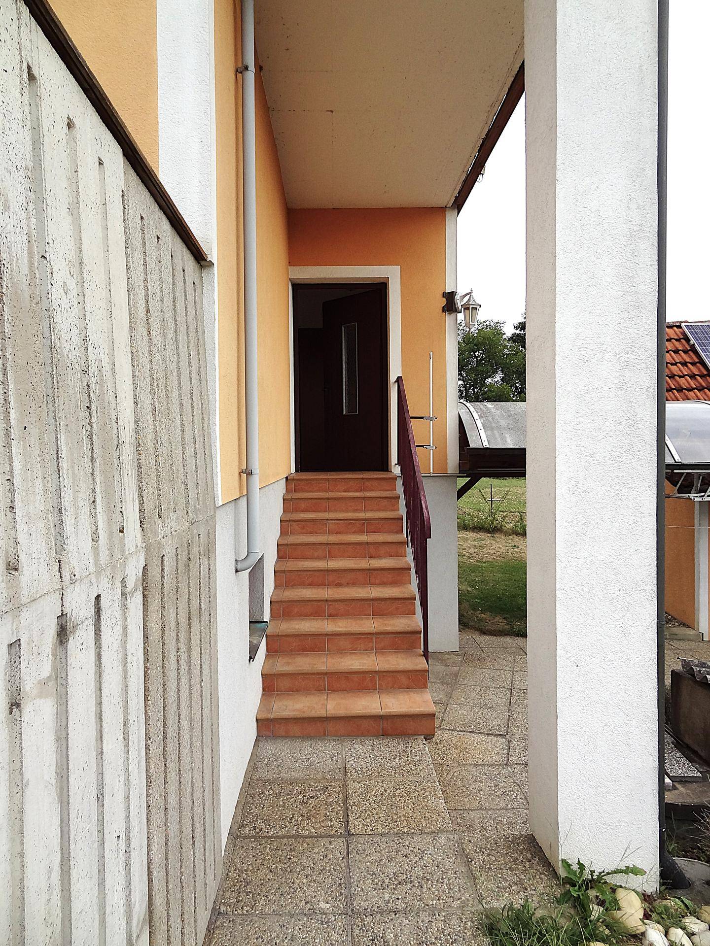 Eingangsbereich mit gefliesten Stufen und Säulen, führt zu einer dunklen Haustür.