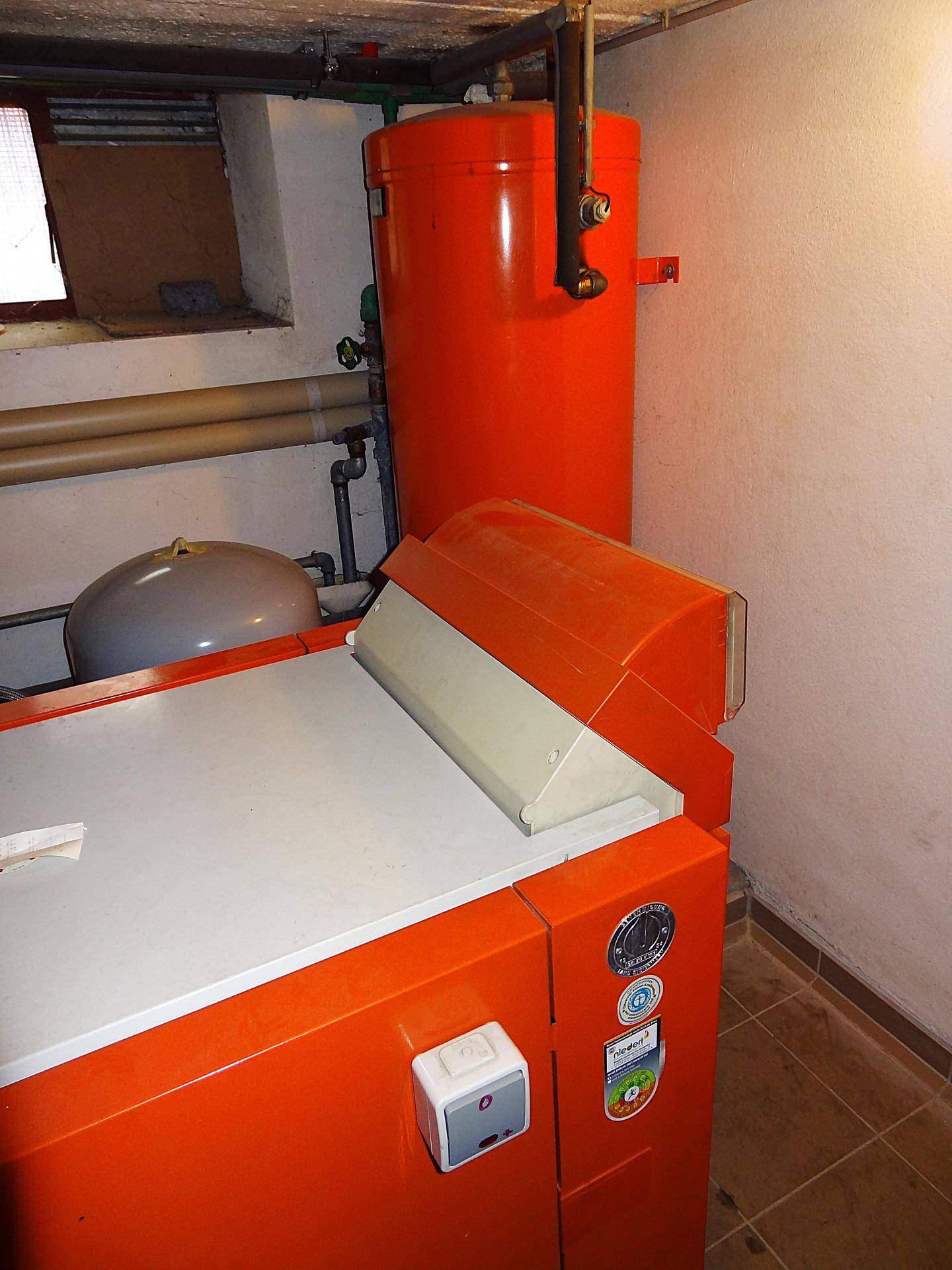 Detailansicht des Heizkessels und eines roten Warmwasserspeichers im Technikraum.