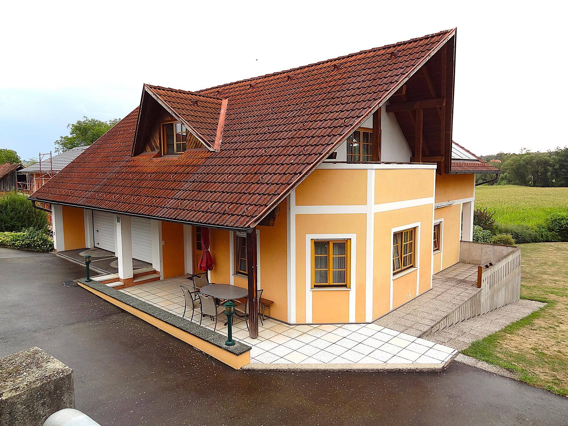 Hausansicht mit Terrasse und angrenzendem Gartenbereich, umgeben von grünen Feldern.