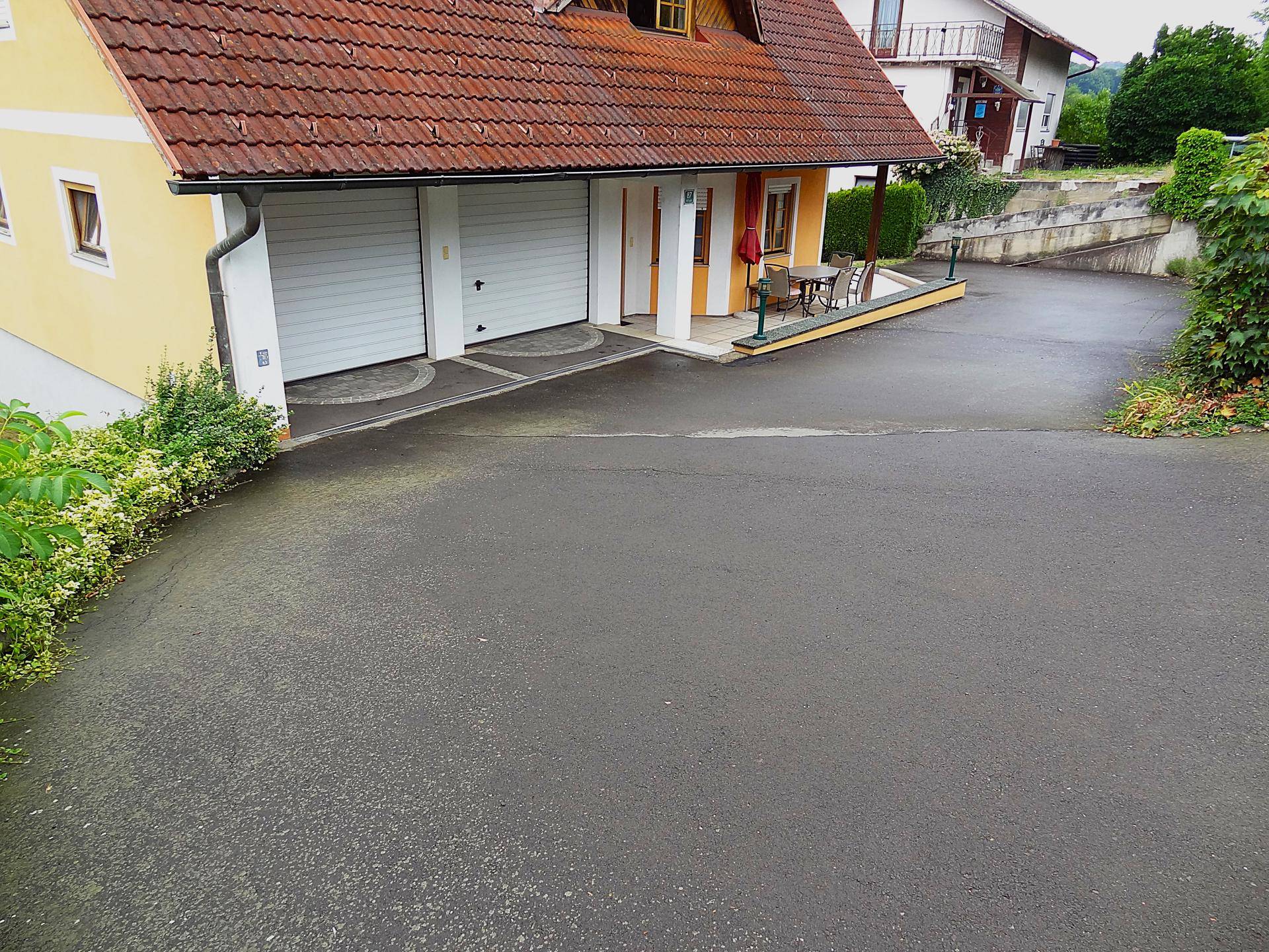 Zufahrt zum Haus mit Doppelgarage und einem kleinen Außenbereich mit Sitzgelegenheiten.