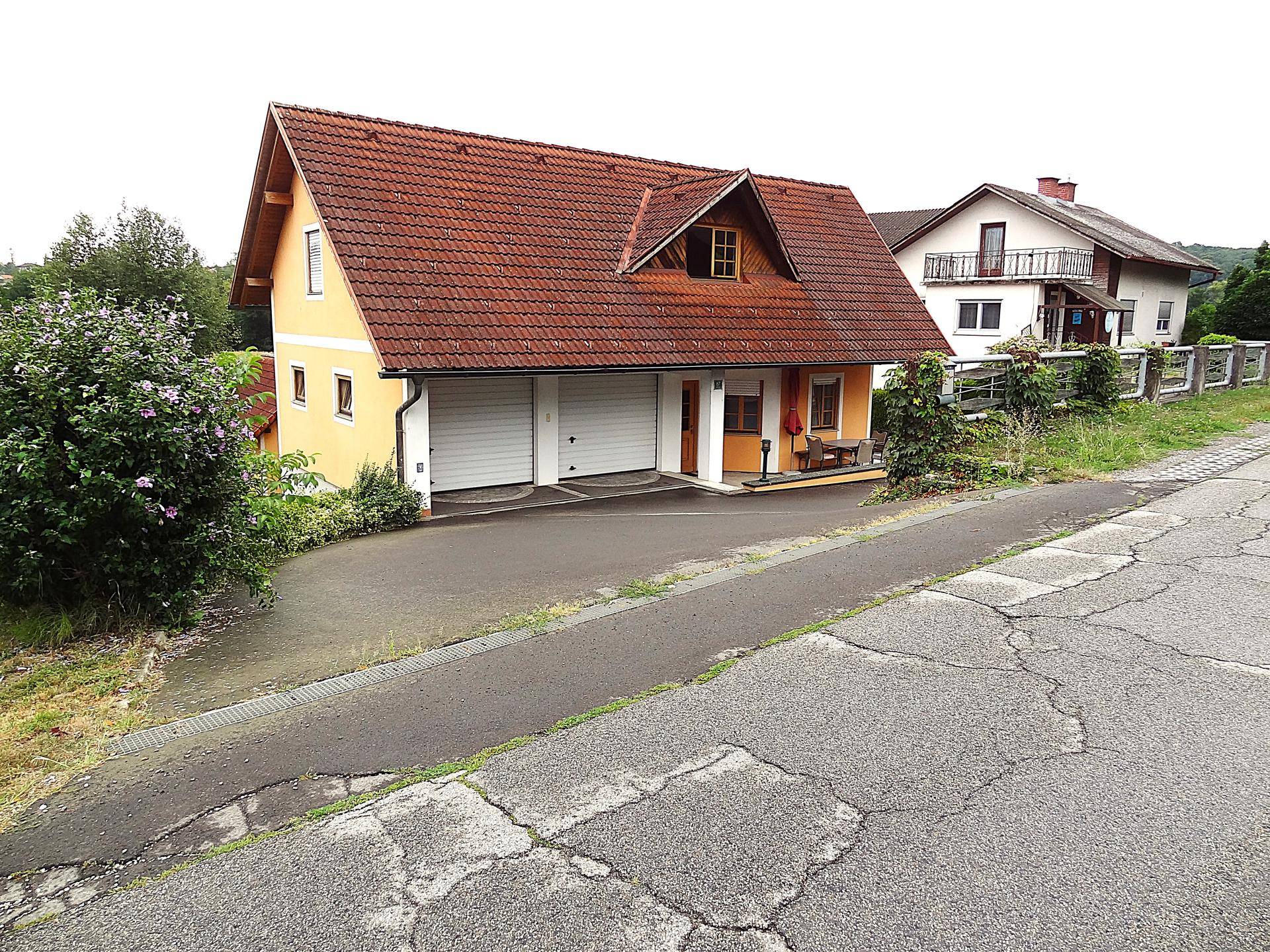 Einfamilienhaus mit rotem Ziegeldach, gelber Fassade und Doppelgarage an einer Straße.