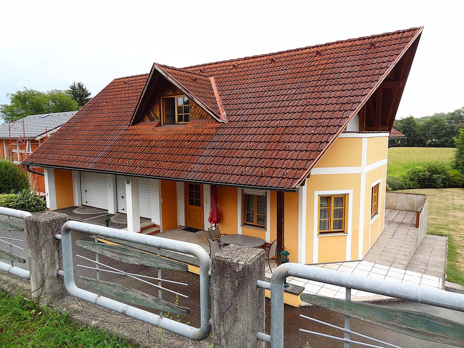 Seitenansicht des Hauses mit gelber Fassade, rotem Dach und einer kleinen Terrasse mit Gartenmöbeln.