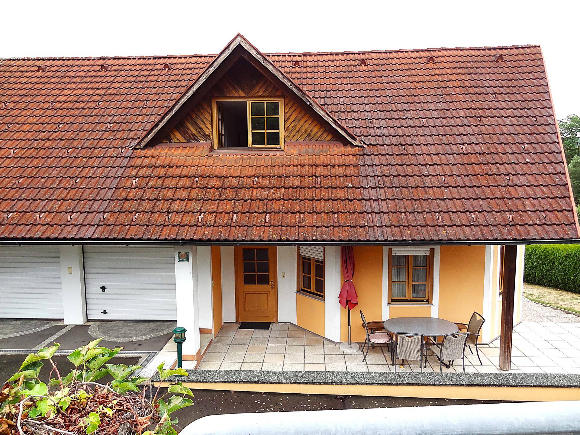 Vorderansicht des Hauses mit Eingangsbereich, möblierter Terrasse und Doppelgarage.