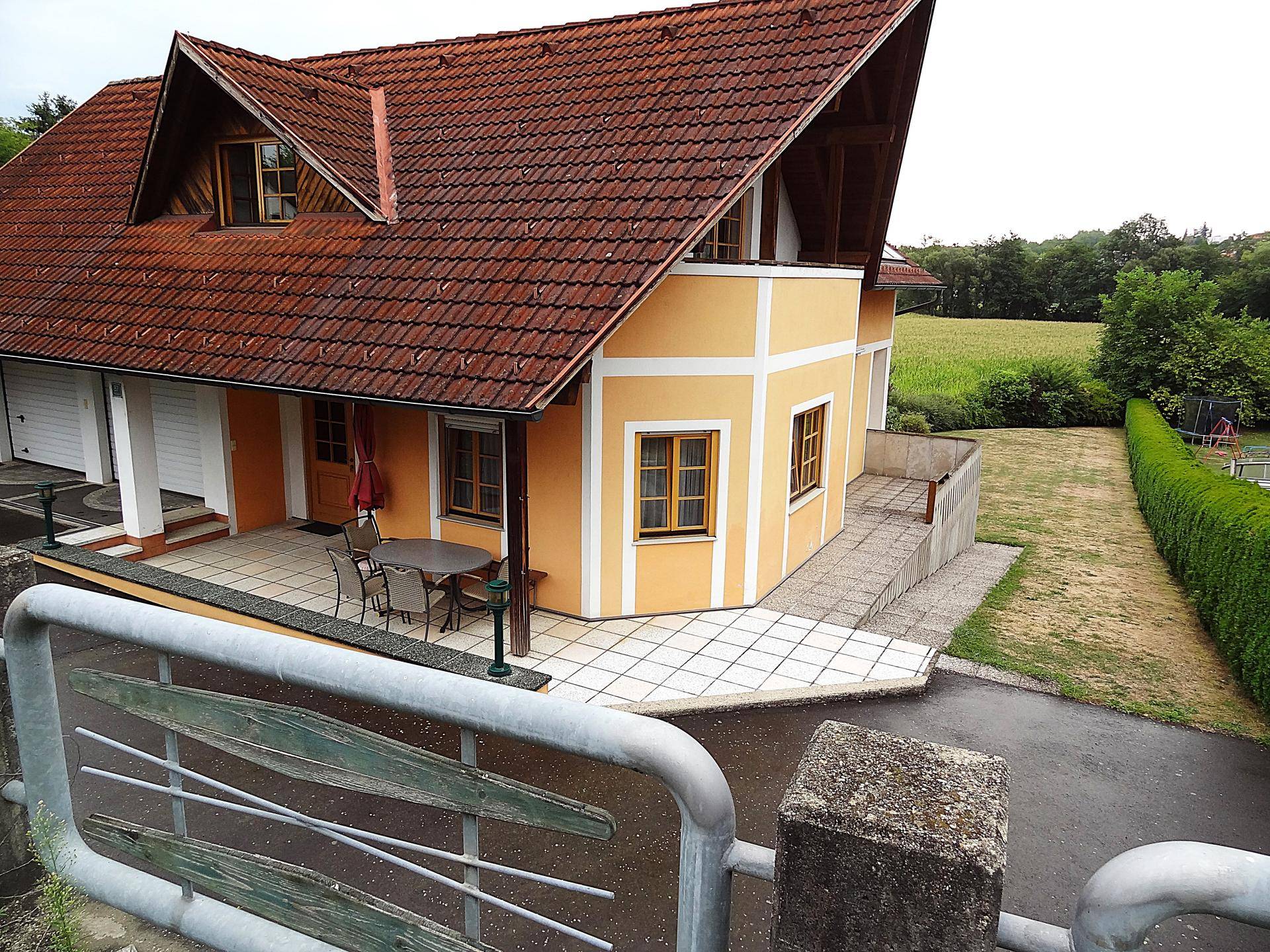 Seitenansicht des Hauses mit Terrasse, gepflegter Hecke und weitem Blick ins Grüne.