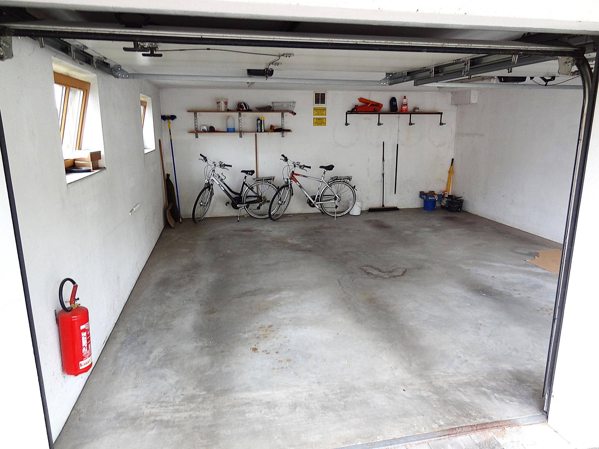 Geräumige Garage mit Betonboden, Fenstern und Abstellmöglichkeiten für Fahrräder.
