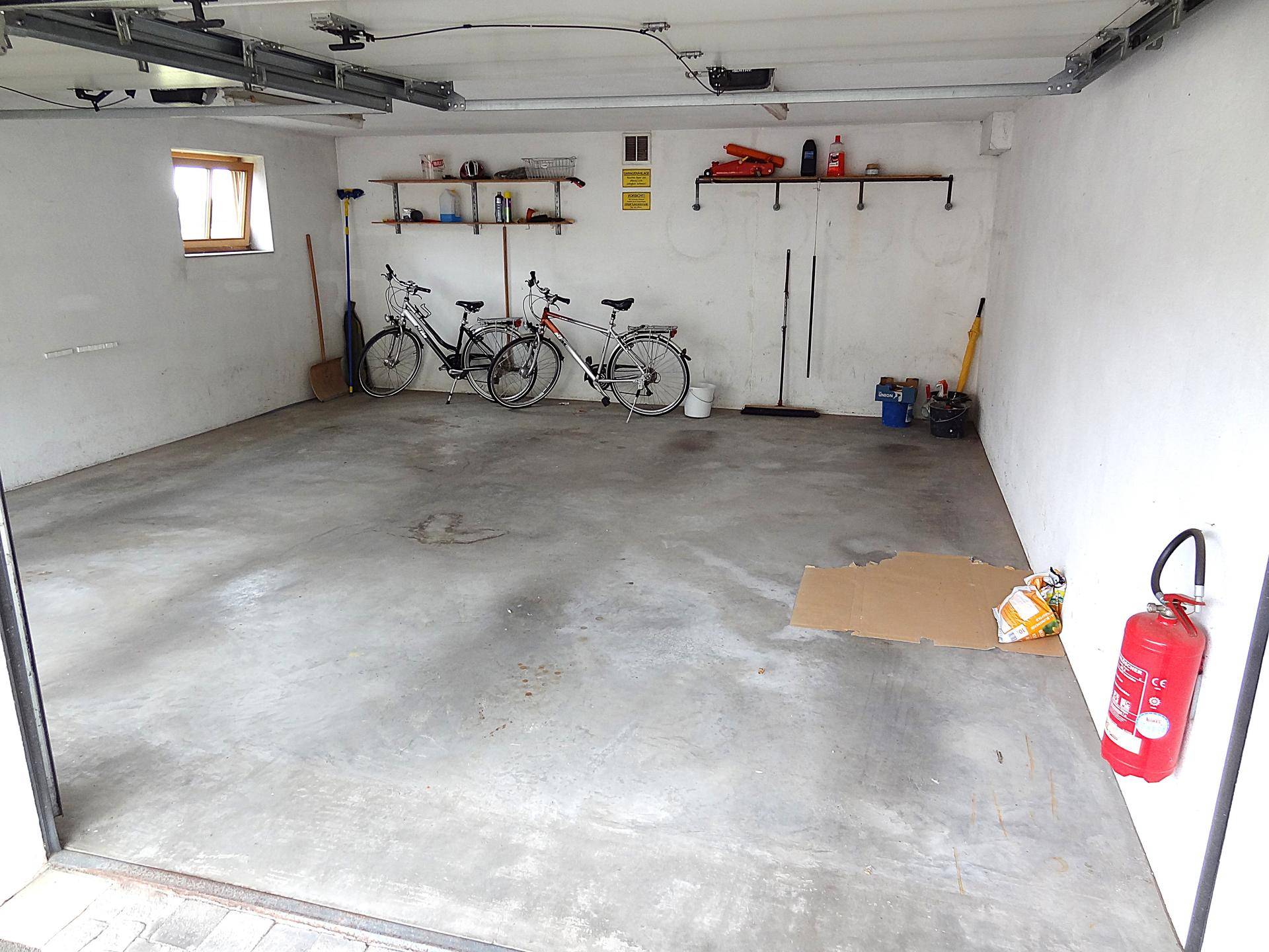 Helle Garage mit viel Platz, Betonboden und Regalen für Werkzeuge und Fahrräder.