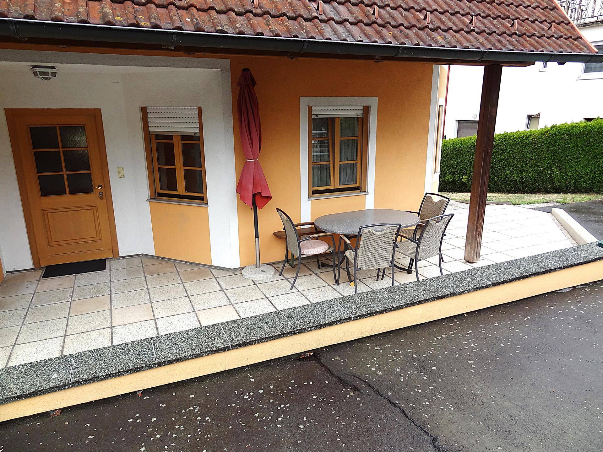 Geflieste Terrasse mit Gartenmöbeln, Sonnenschirm und Zugang zum Haus.