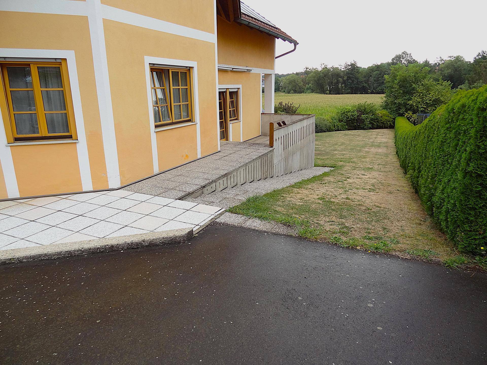 Seitenansicht des Hauses mit barrierefreier Rampe und gepflegter Hecke.
