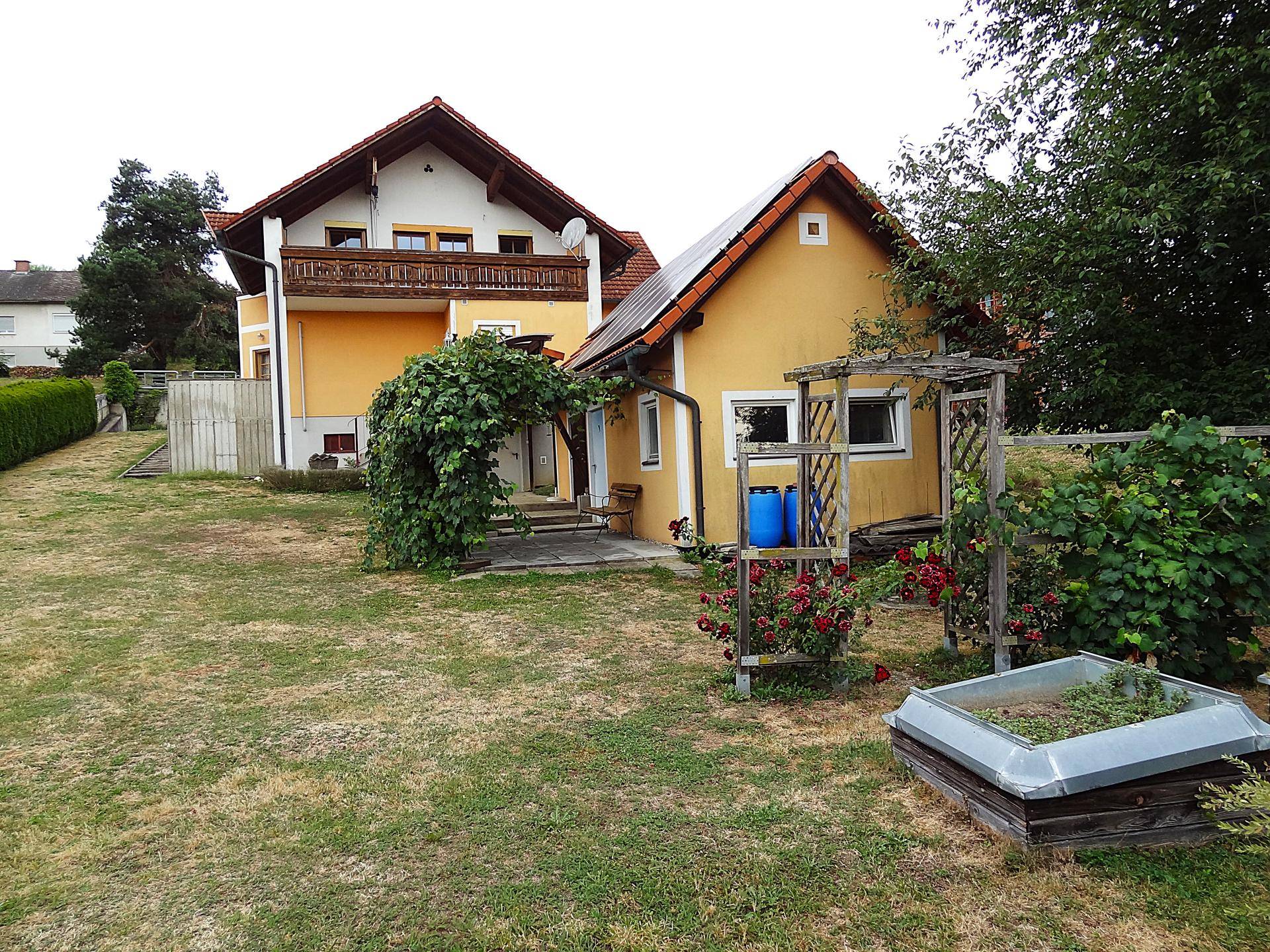 Garten mit Nebengebäude, Rosen und dem Haupthaus im Hintergrund.