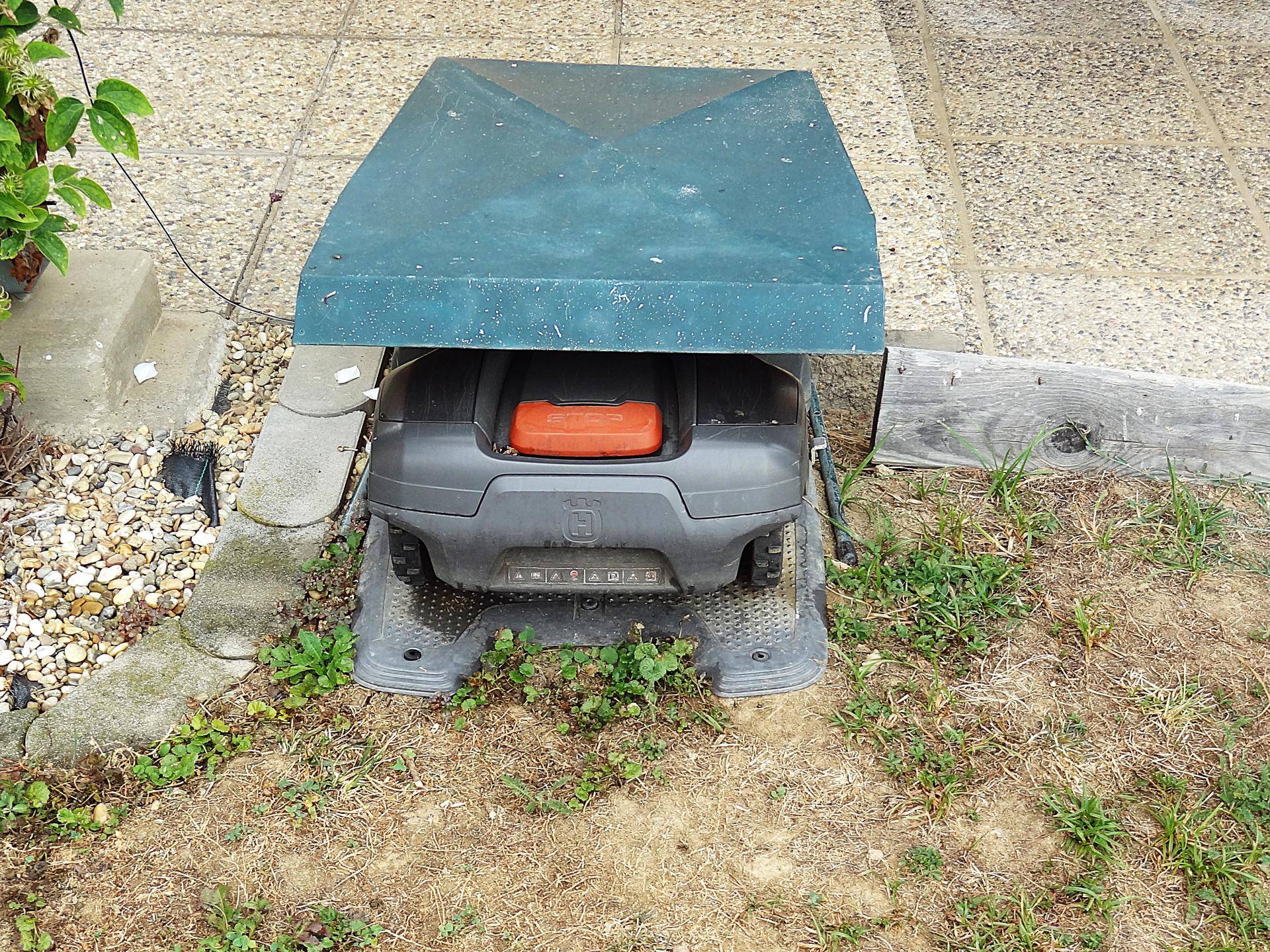Ladestation für einen Mähroboter im Gartenbereich, umgeben von Gras.