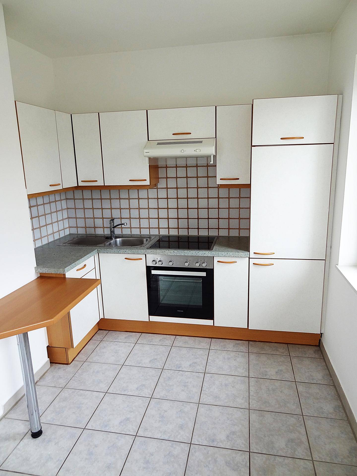 Funktionale Einbauküche mit weißen Fronten, grauer Arbeitsplatte und gefliestem Boden.