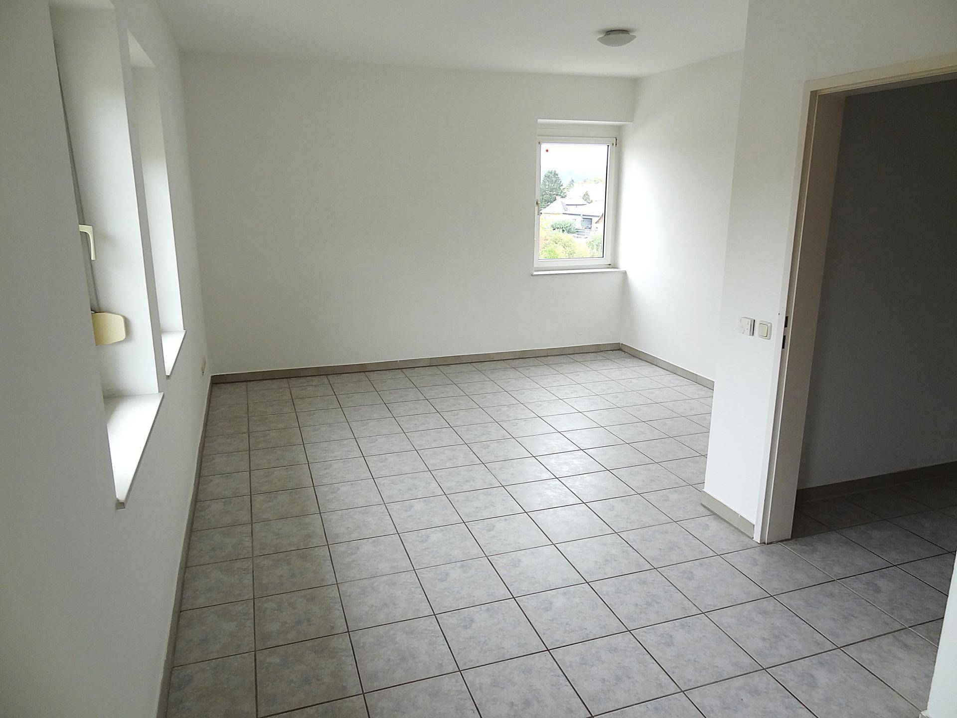 Leeres Zimmer mit hellen Fliesen, weißen Wänden und einem Fenster mit Ausblick.