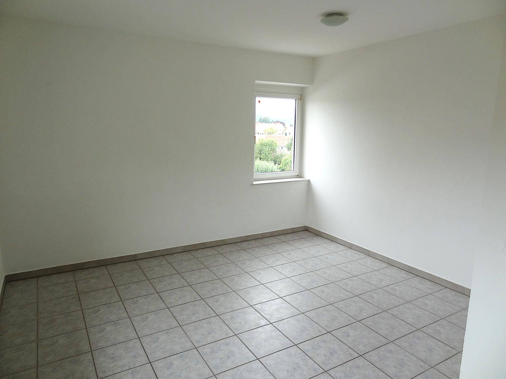 Helles, unmöbliertes Zimmer mit Fliesenboden und einem Fenster, das viel Licht hereinlässt.
