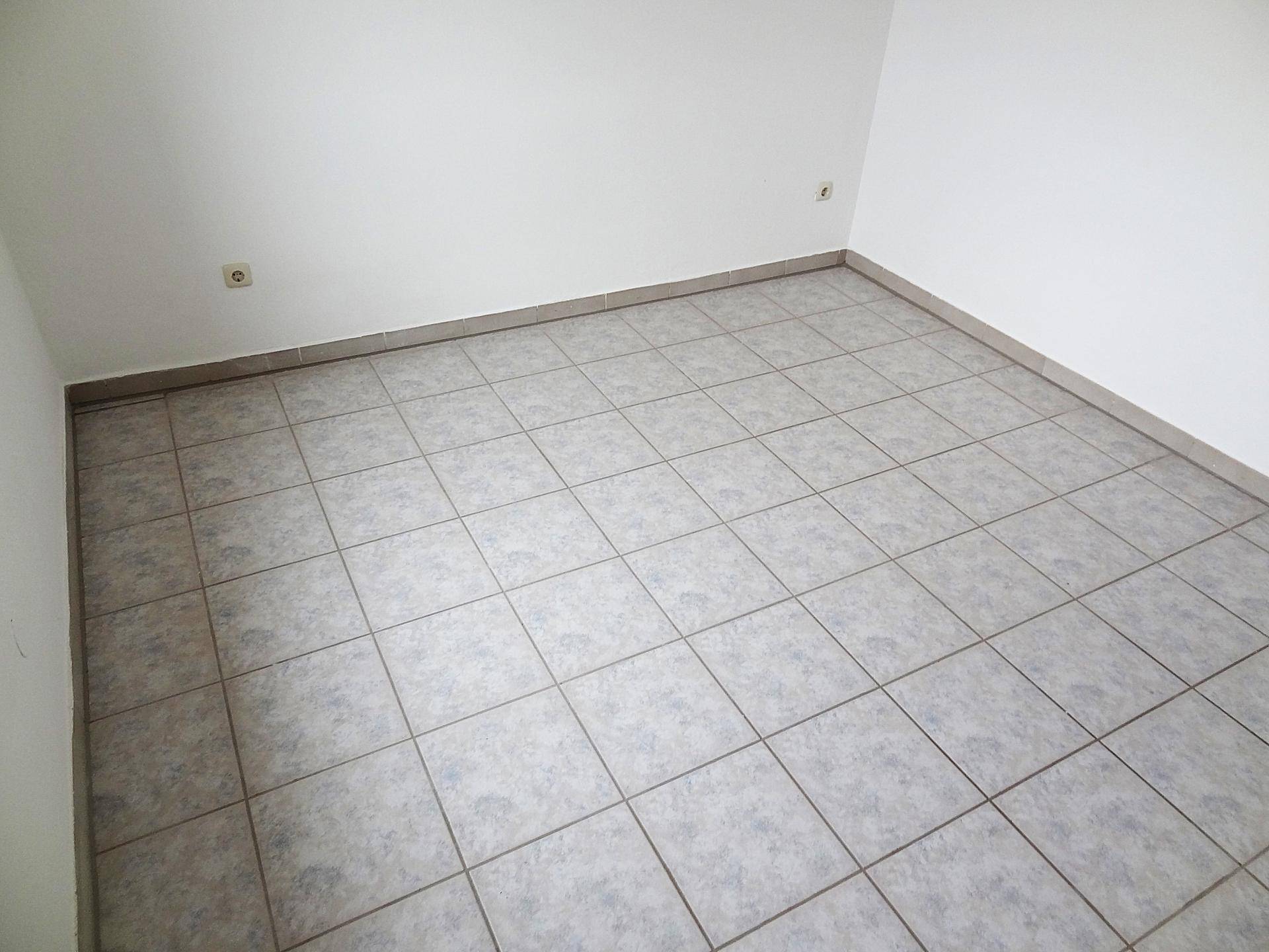 Leerer Raum mit hellgrauen Fliesen und weißen Wänden, ideal für ein Schlafzimmer oder Büro.