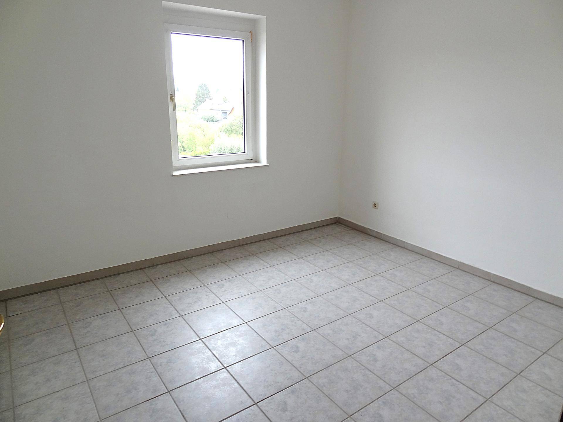 Helles Zimmer mit Fliesenboden und einem Fenster, das einen Blick ins Freie ermöglicht.