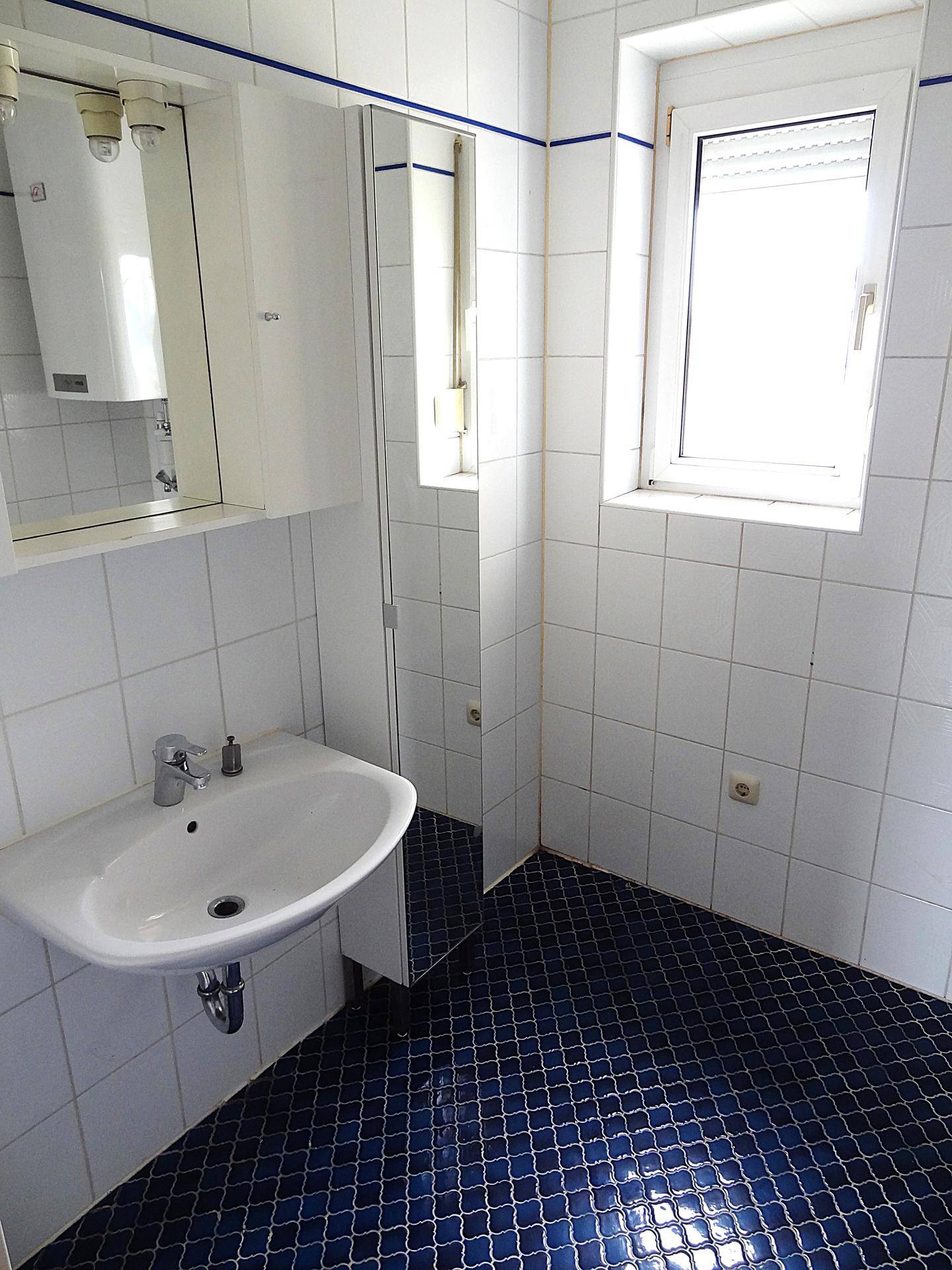 Badezimmer mit weißen Wandfliesen, blauem Boden und einem Waschbecken mit Spiegelschrank.