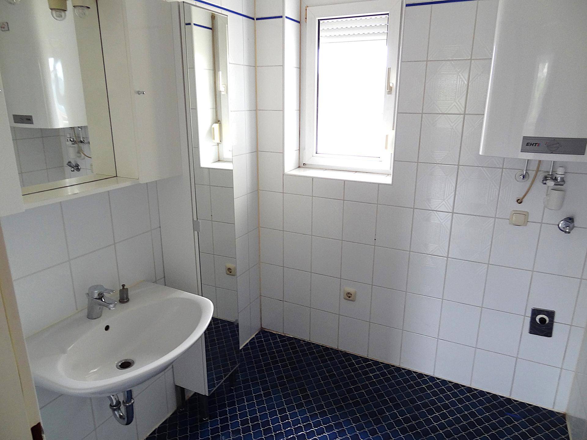 Badezimmer mit weißen Wandfliesen, blauem Boden und einem Waschbecken mit Spiegelschrank.