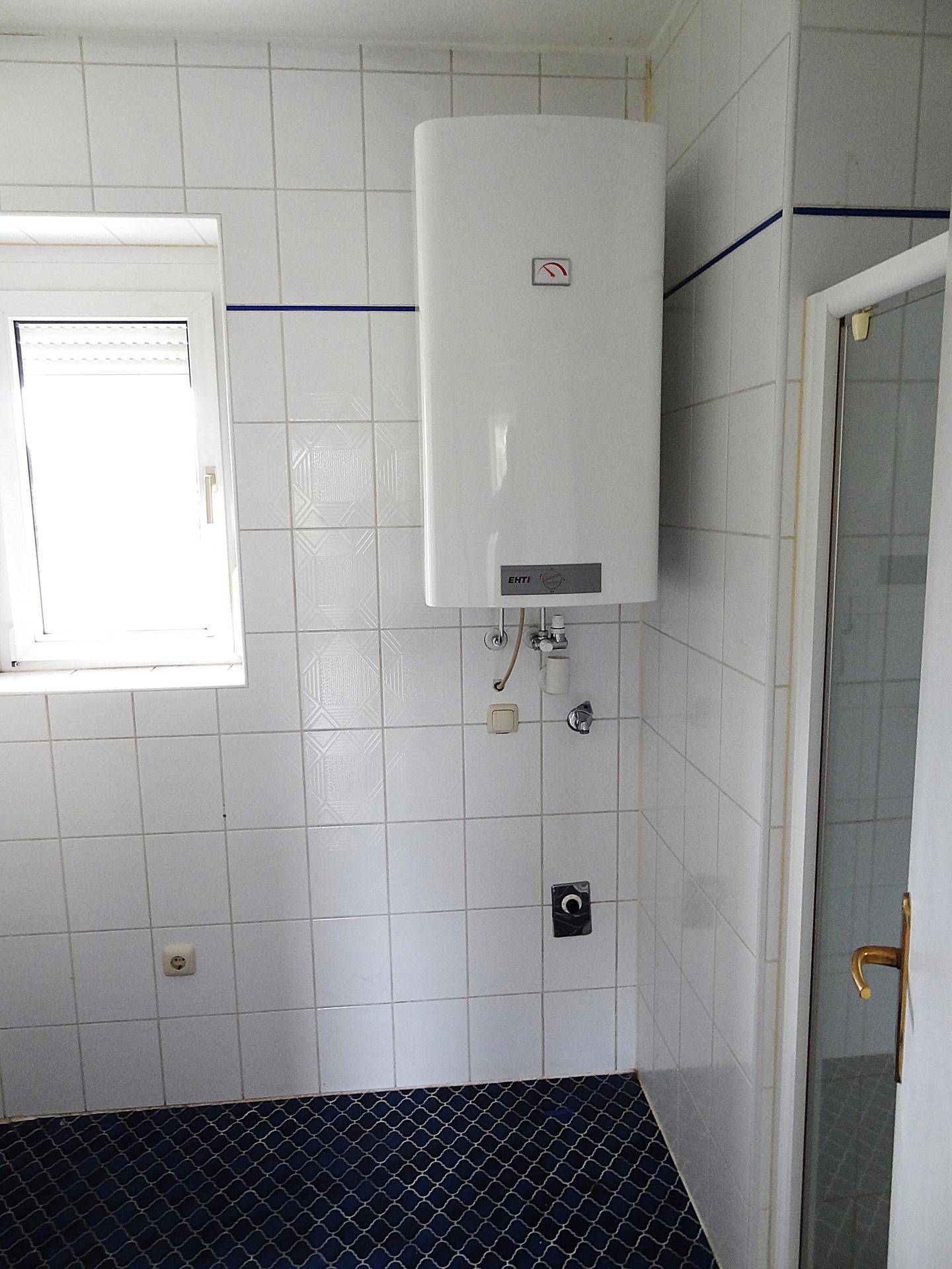 Badezimmer mit weiß gefliesten Wänden, blauem Boden und einem Warmwasserboiler.