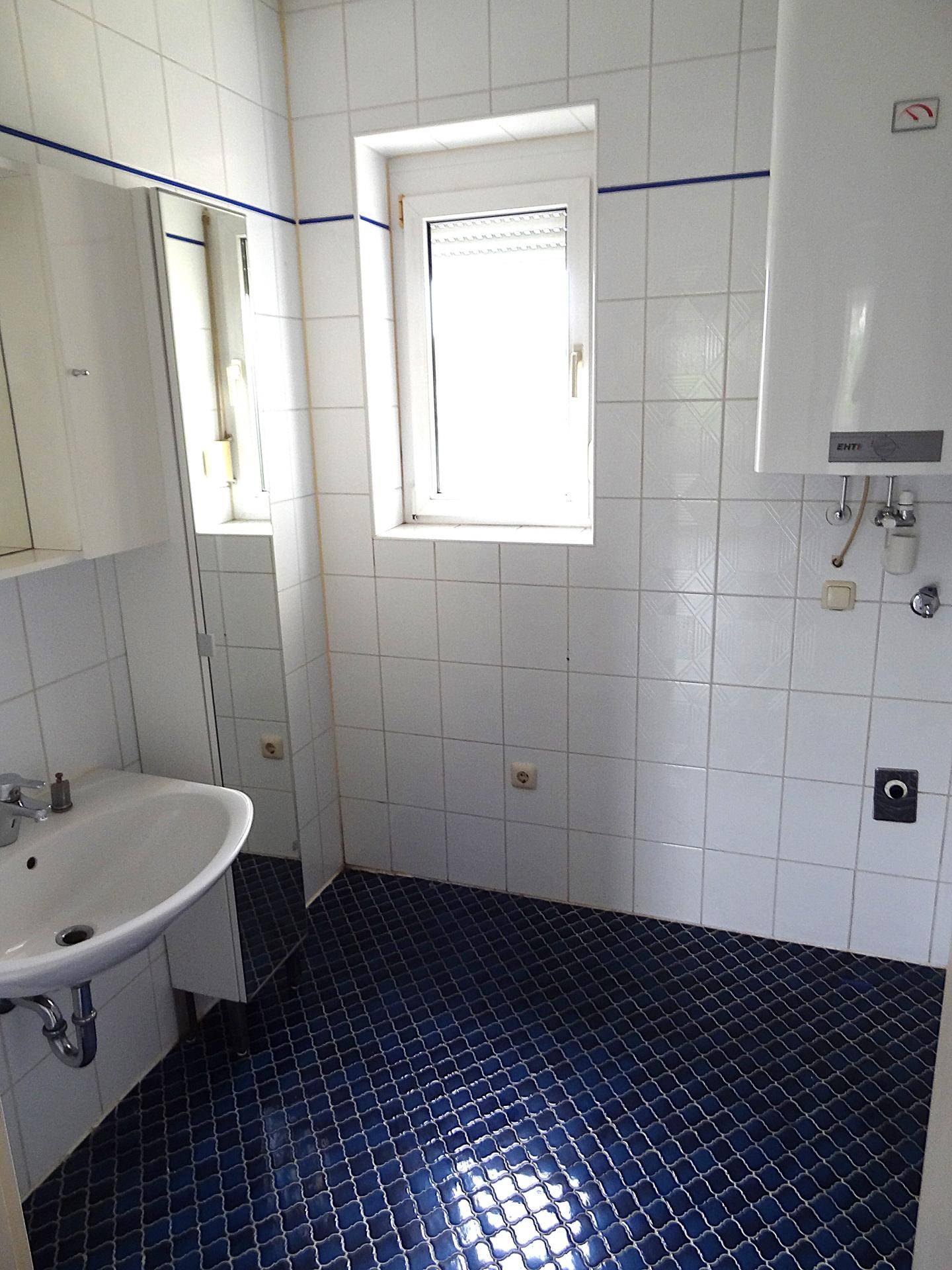 Badezimmer mit weißen Wandfliesen, blauem Boden und einem Fenster für Tageslicht.