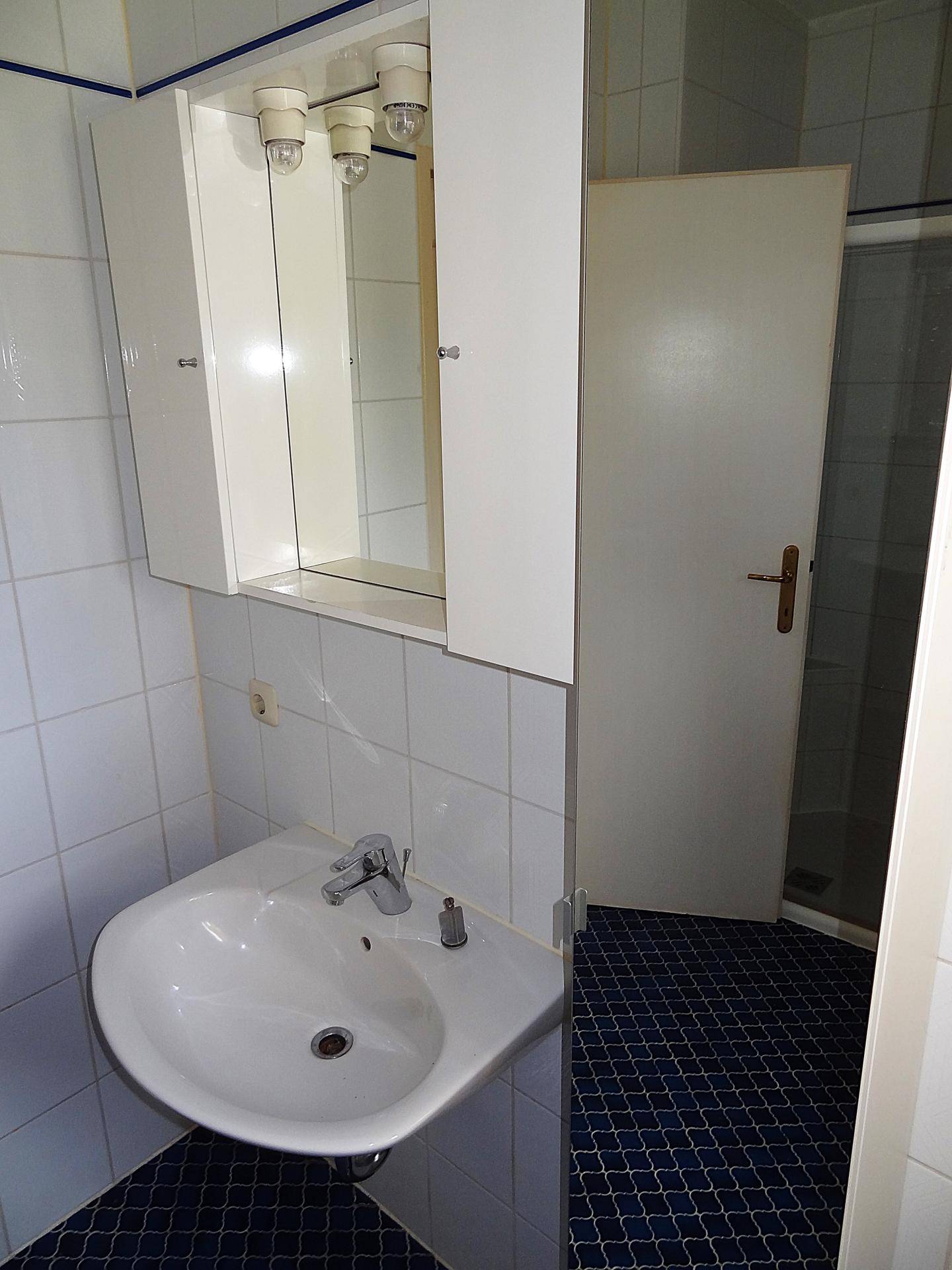Funktionales Badezimmer mit Waschbecken, Spiegelschrank und Duschkabine, ausgestattet mit weißen Wandfliesen.