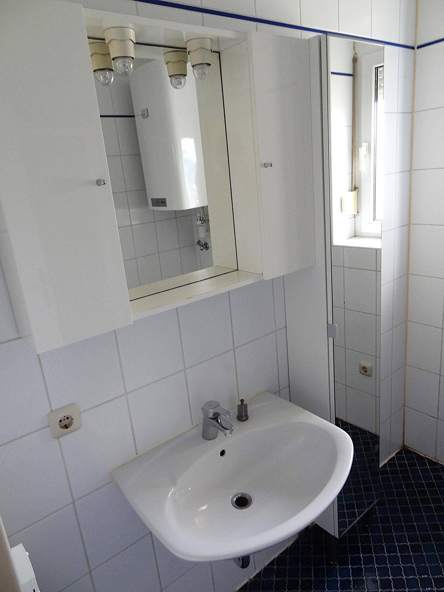 Badezimmer mit Waschbecken, Spiegelschrank und einem Fenster, das für natürliches Licht sorgt.