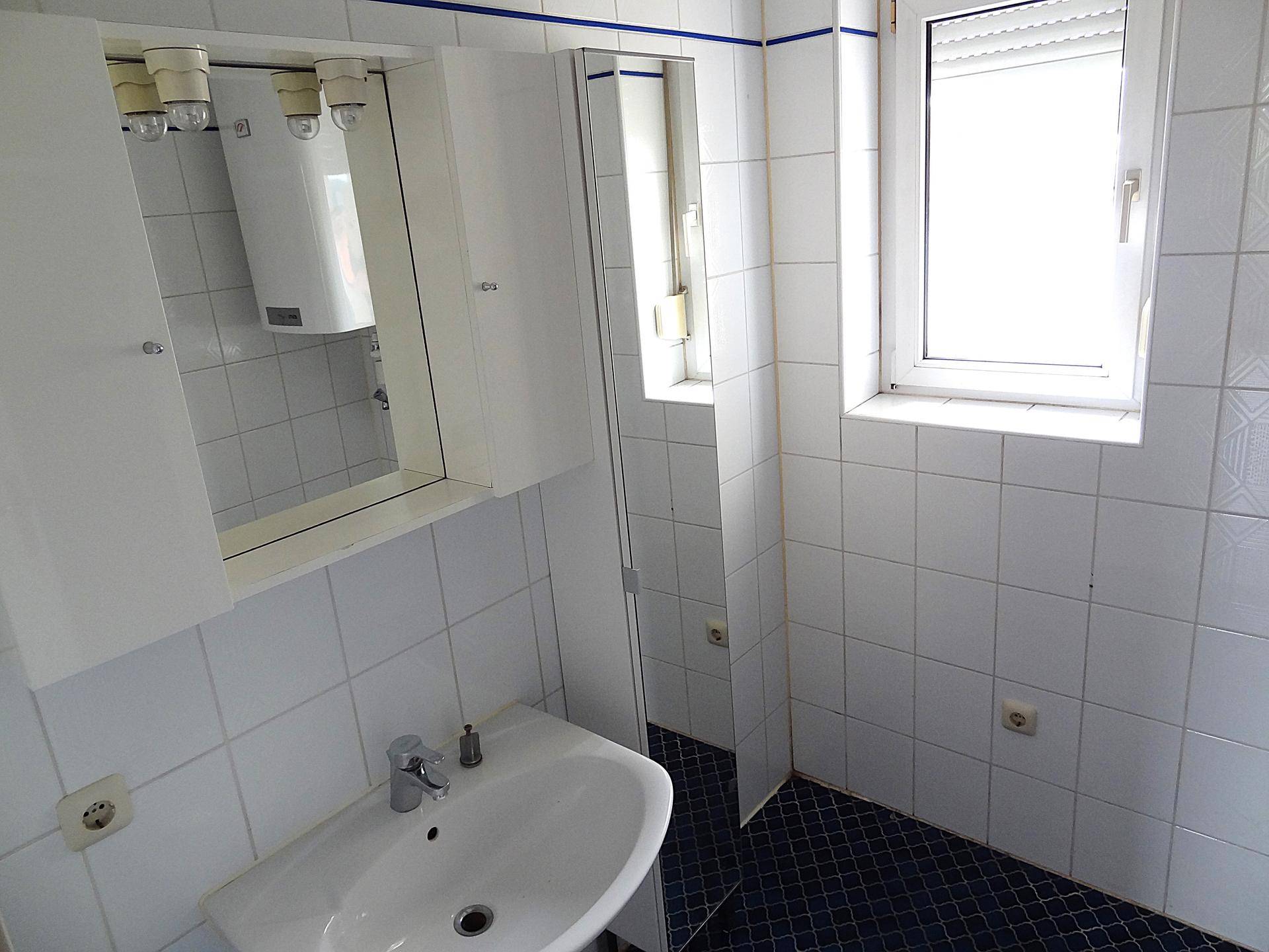 Helles Badezimmer mit Waschbecken, Spiegelschrank und einem großen Fenster für gute Belüftung.