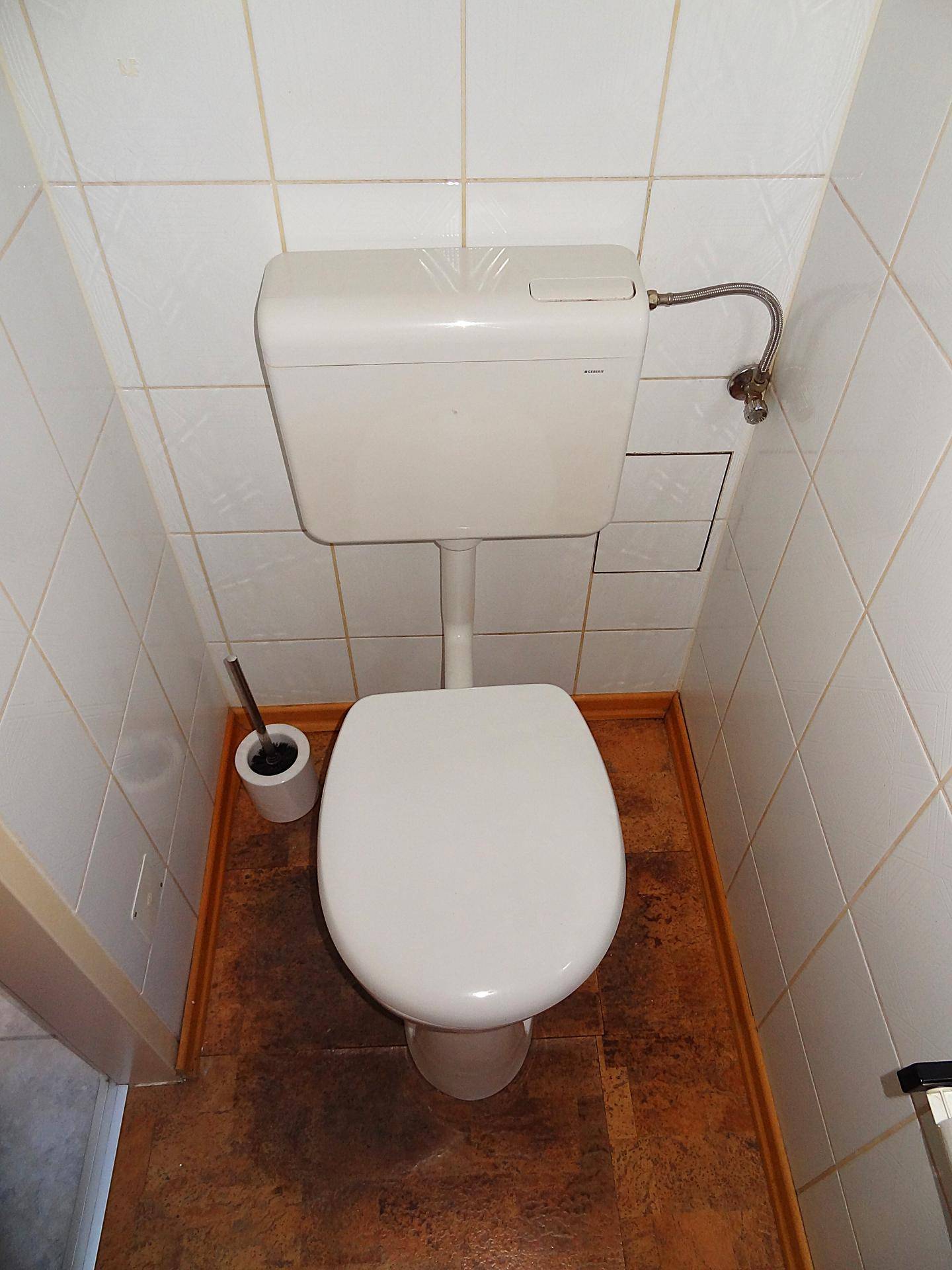 Kleines WC mit Toilette, weißen Wandfliesen und einem braunen Bodenbelag, einfach gehalten.