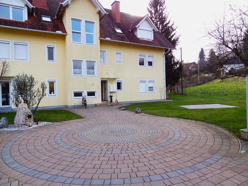 Gelbes Gebäude mit einem kreisförmig gepflasterten Vorplatz und einer gepflegten Rasenfläche.