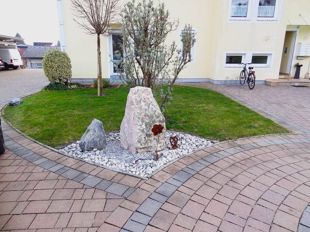 Vorgartenbereich mit dekorativen Steinen, Kies und Rasenfläche, umgeben von einem gepflasterten Weg.