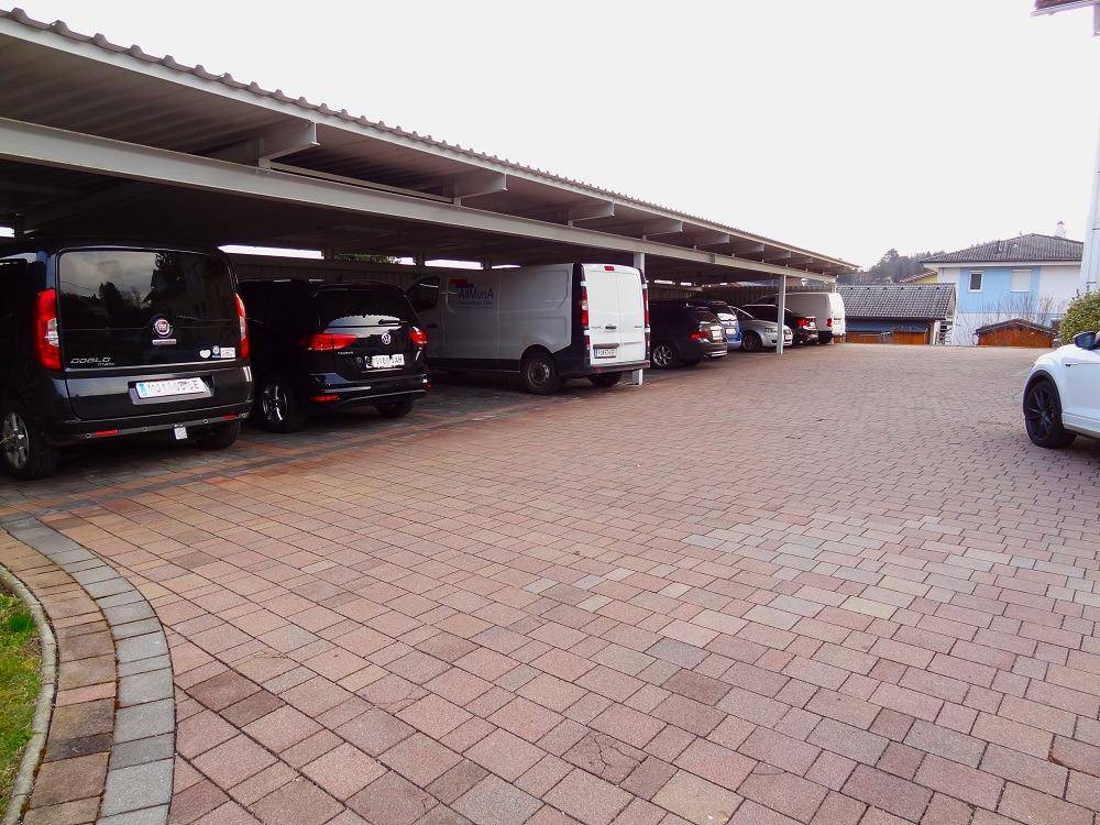 Überdachter Carportbereich mit mehreren geparkten Fahrzeugen auf einem gepflasterten Untergrund.