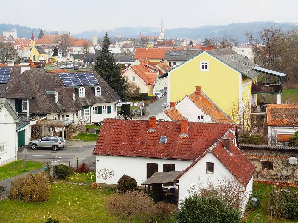 Übersicht einer Wohnsiedlung mit traditionellen Häusern, grünen Gärten und hügeliger Landschaft im Hintergrund.