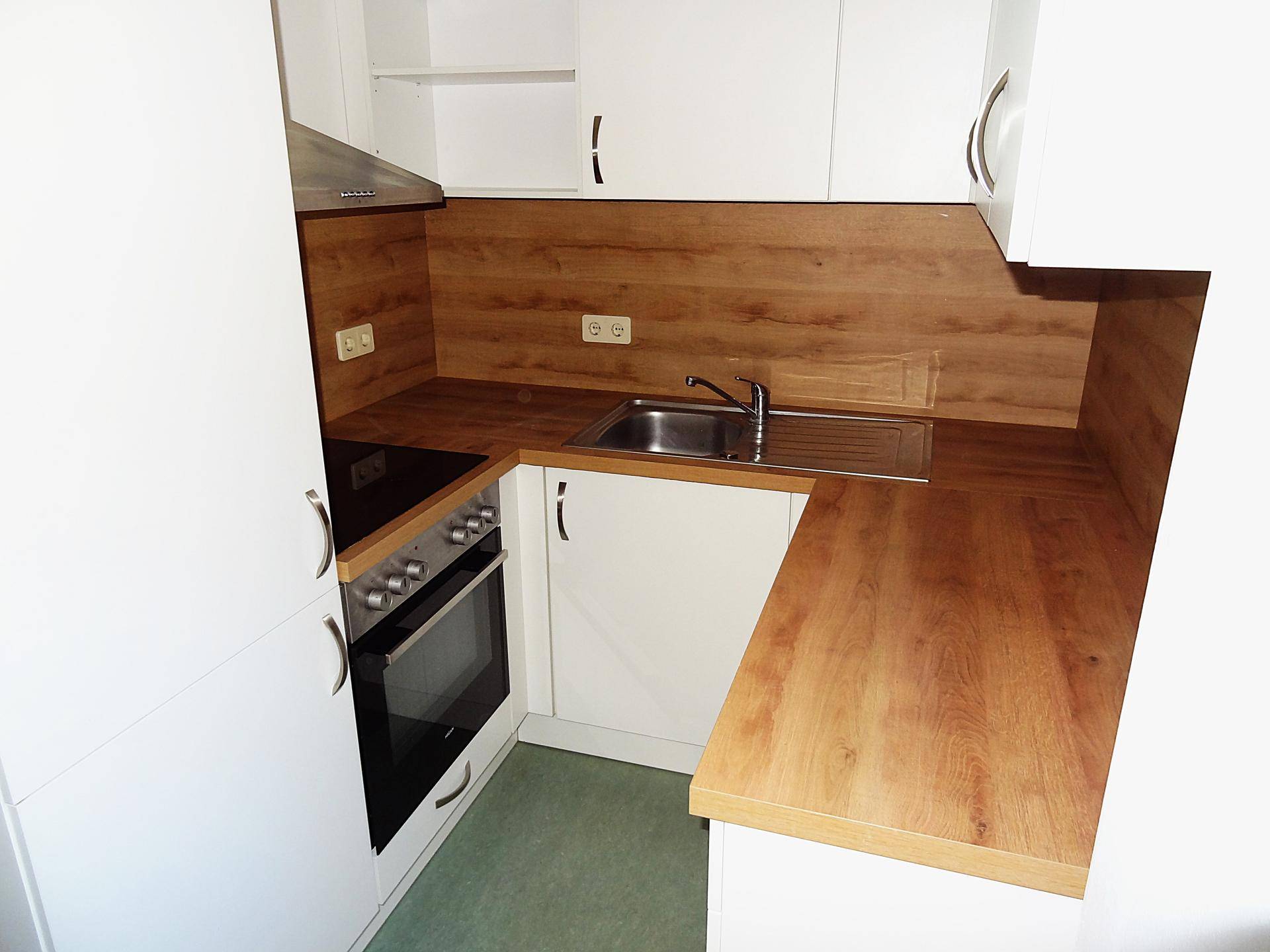 Kompakte Küche mit weißen Oberschränken, Holz-Arbeitsplatte und Herd mit Cerankochfeld.