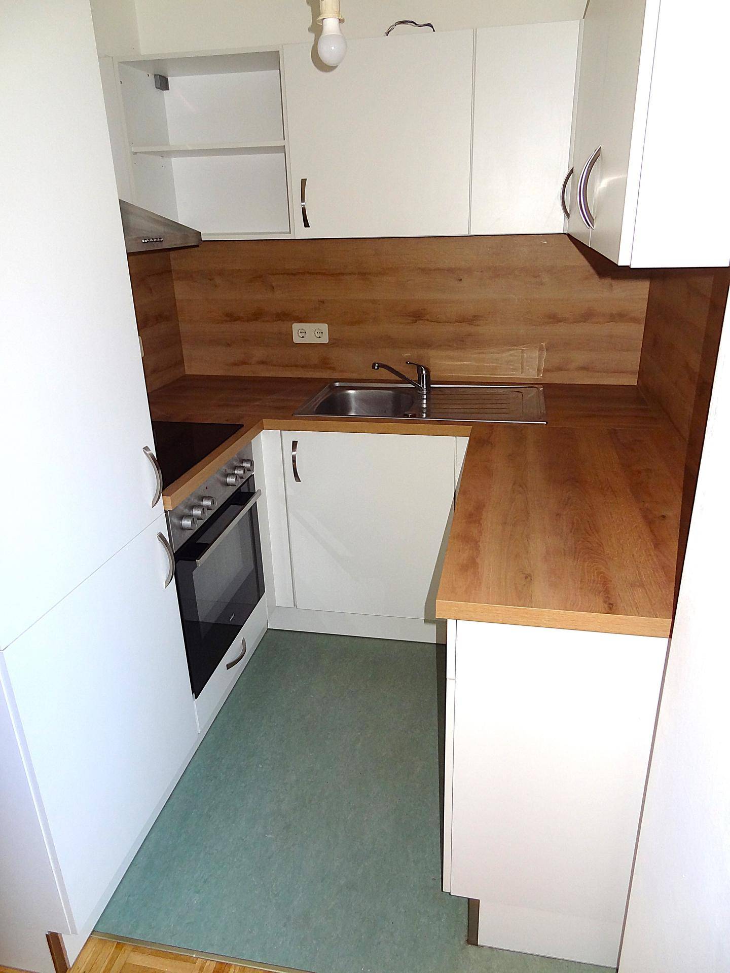 Helle Küche mit weißen Schränken, Holz-Arbeitsflächen und grünem Bodenbelag.