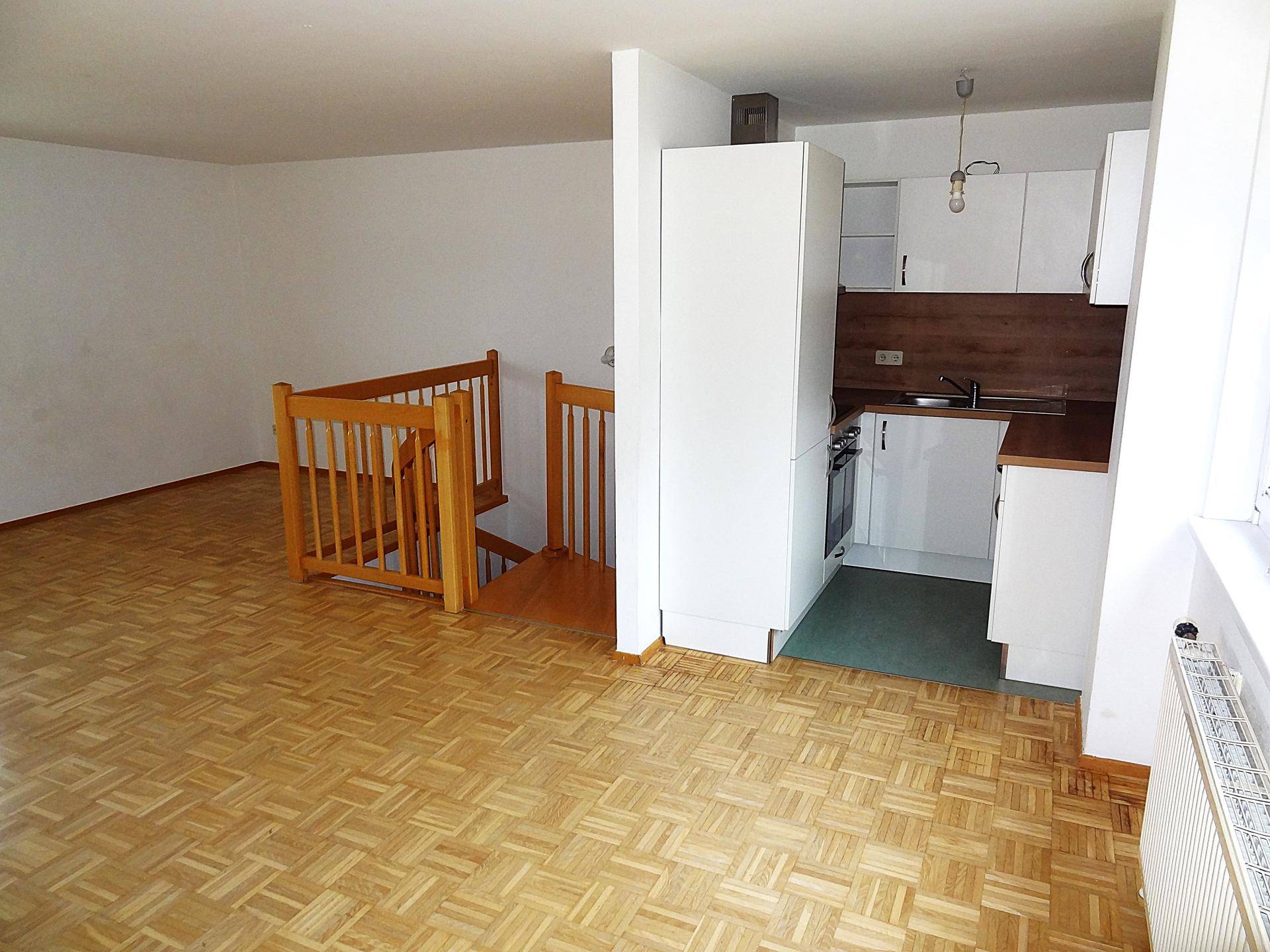 Heller Wohnbereich mit Parkettboden, Holztreppe und offener Küchenzeile im Hintergrund.