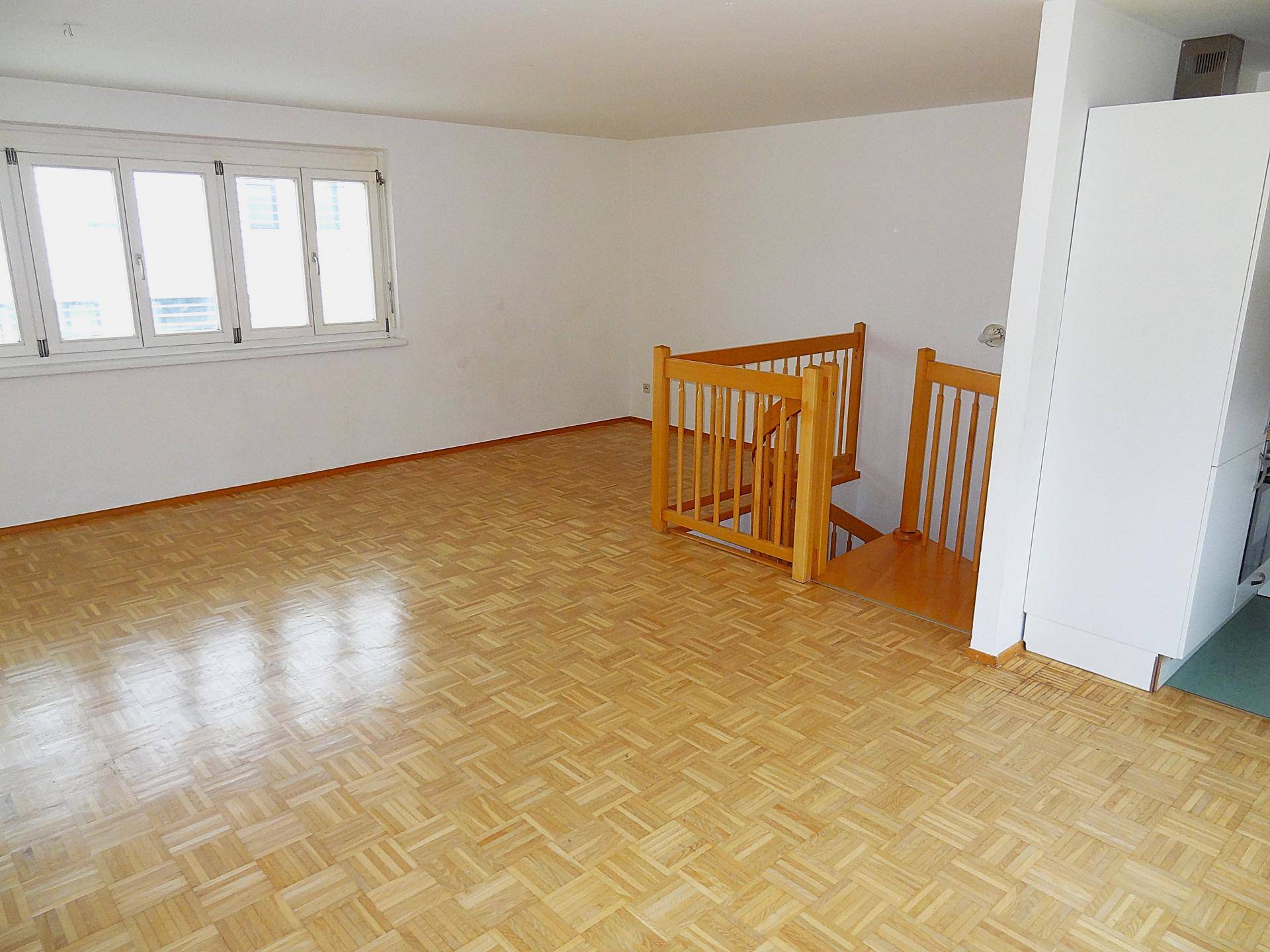 Offener Wohnbereich mit Parkett, Holztreppe und angrenzender Küchenzeile.