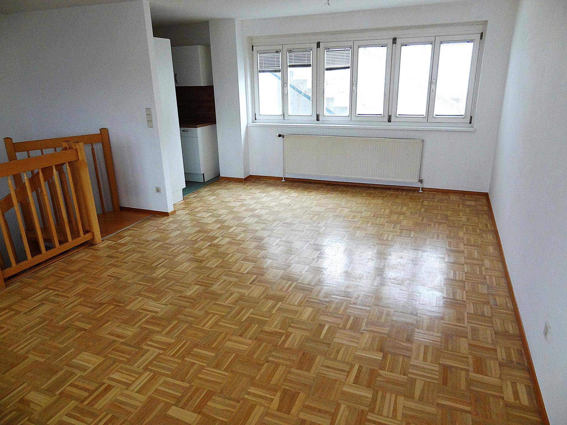 Lichtdurchfluteter Wohnraum mit klassischem Parkettboden und Heizkörper unter dem Fenster.