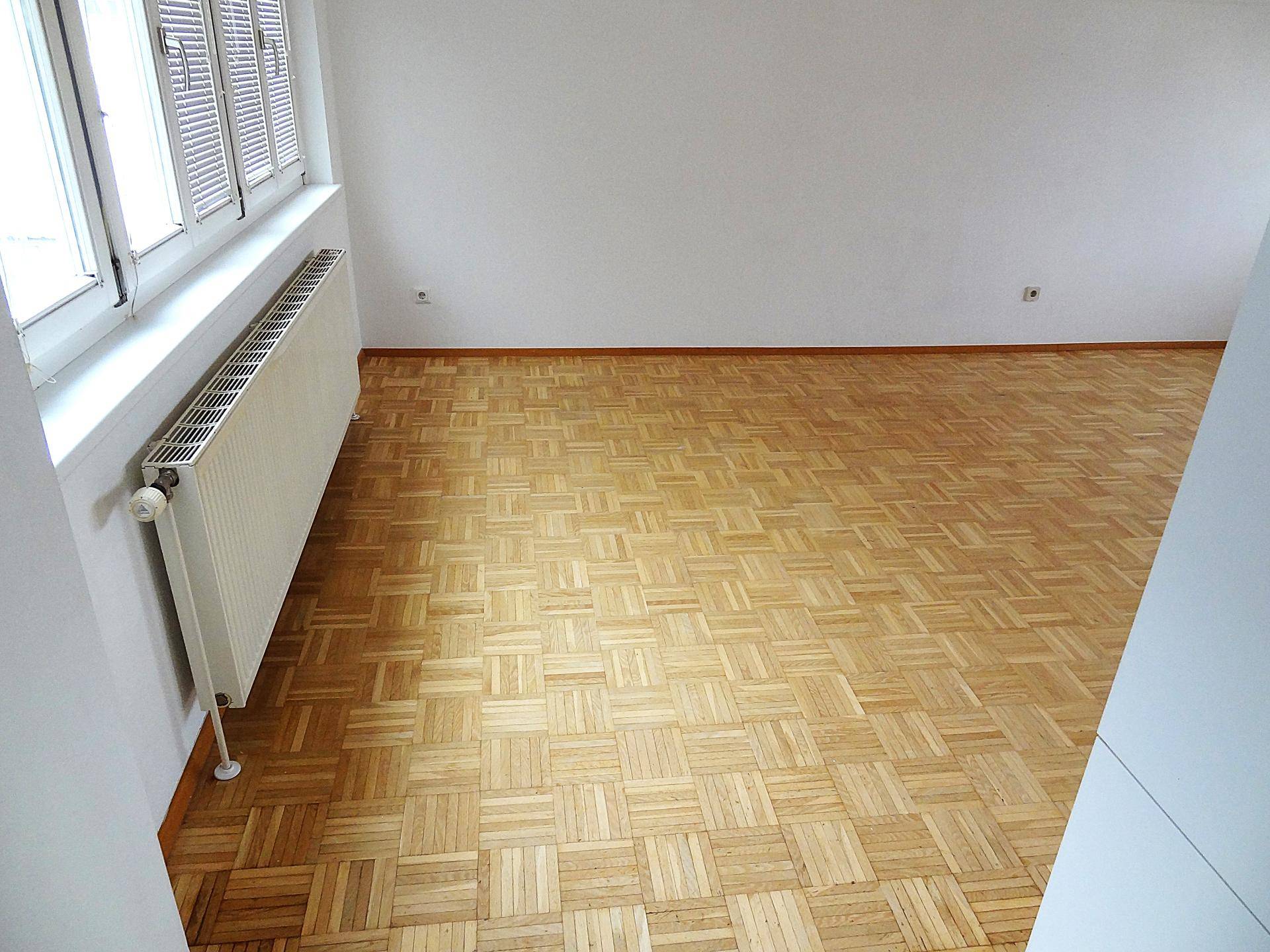 Detailansicht des Parkettbodens und des Heizkörpers unter dem Fenster im Wohnzimmer.