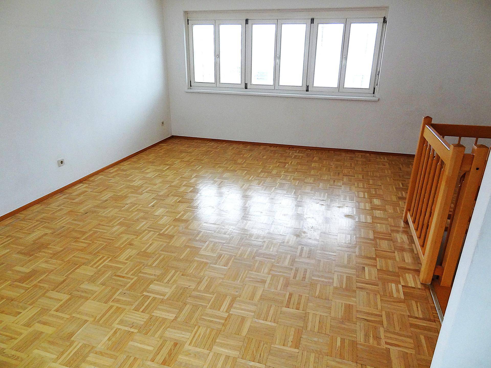 Geräumiger Wohnraum mit hellem Parkettboden und großen Fenstern für viel Tageslicht.