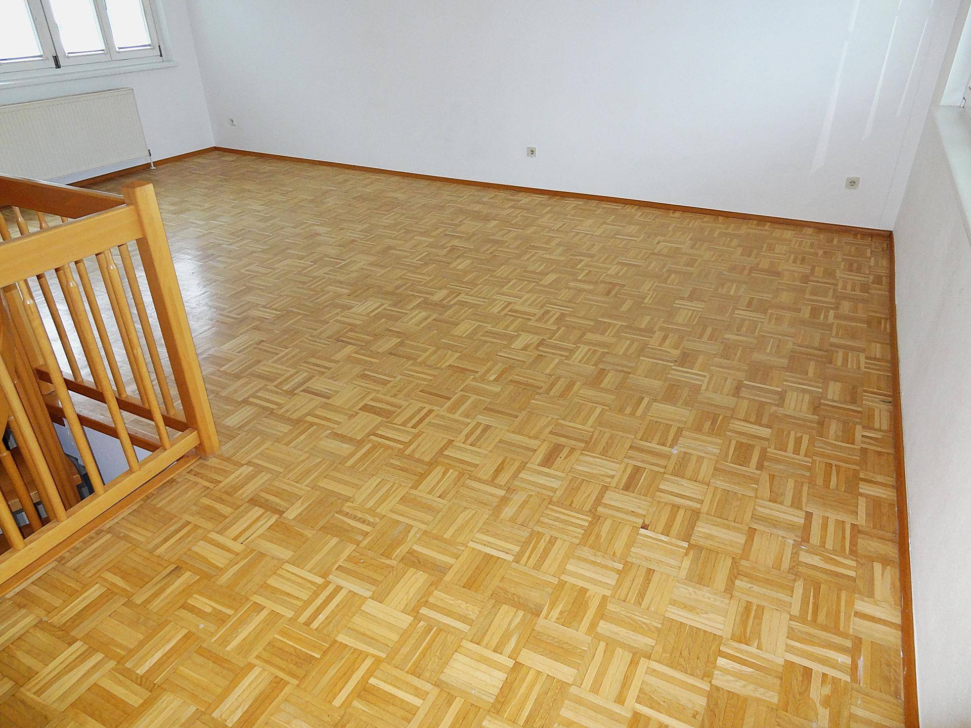 Geräumiger Wohnraum mit Parkettboden und Holztreppe, die den Raum strukturiert.