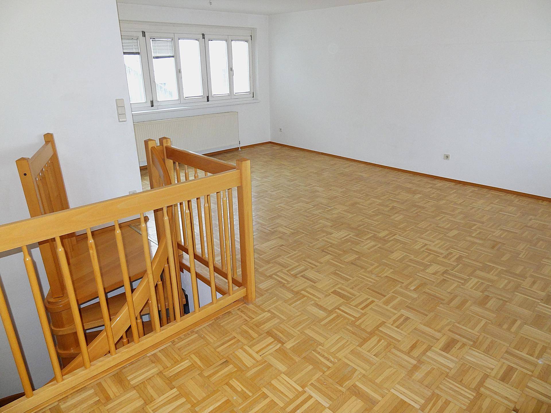 Heller Wohnbereich mit Parkettboden, Fenster und einer eleganten Holztreppe.