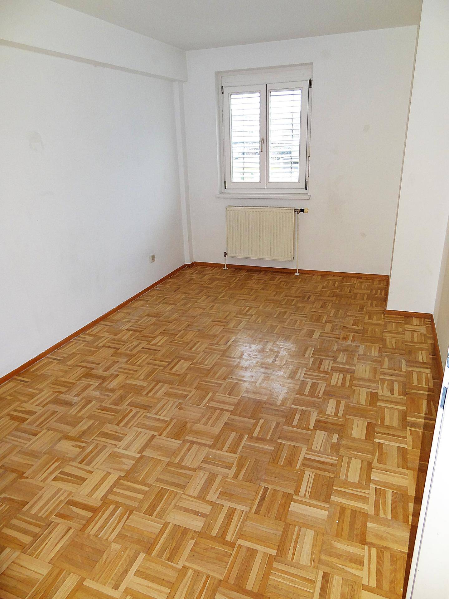 Geräumiges Schlafzimmer mit Parkettboden, viel Tageslicht und Heizkörper unter dem Fenster.