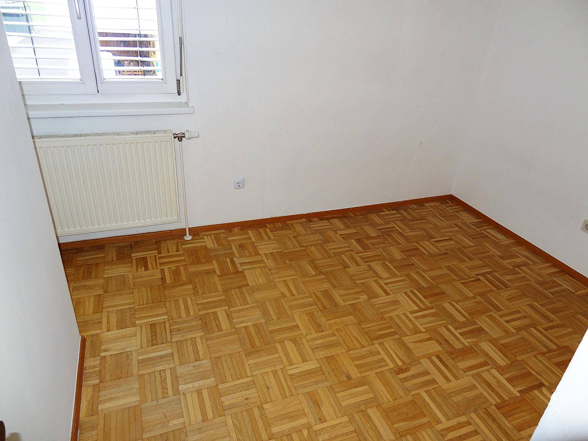 Helles Schlafzimmer mit Parkettboden und Fenster, das für natürliche Belüftung sorgt.